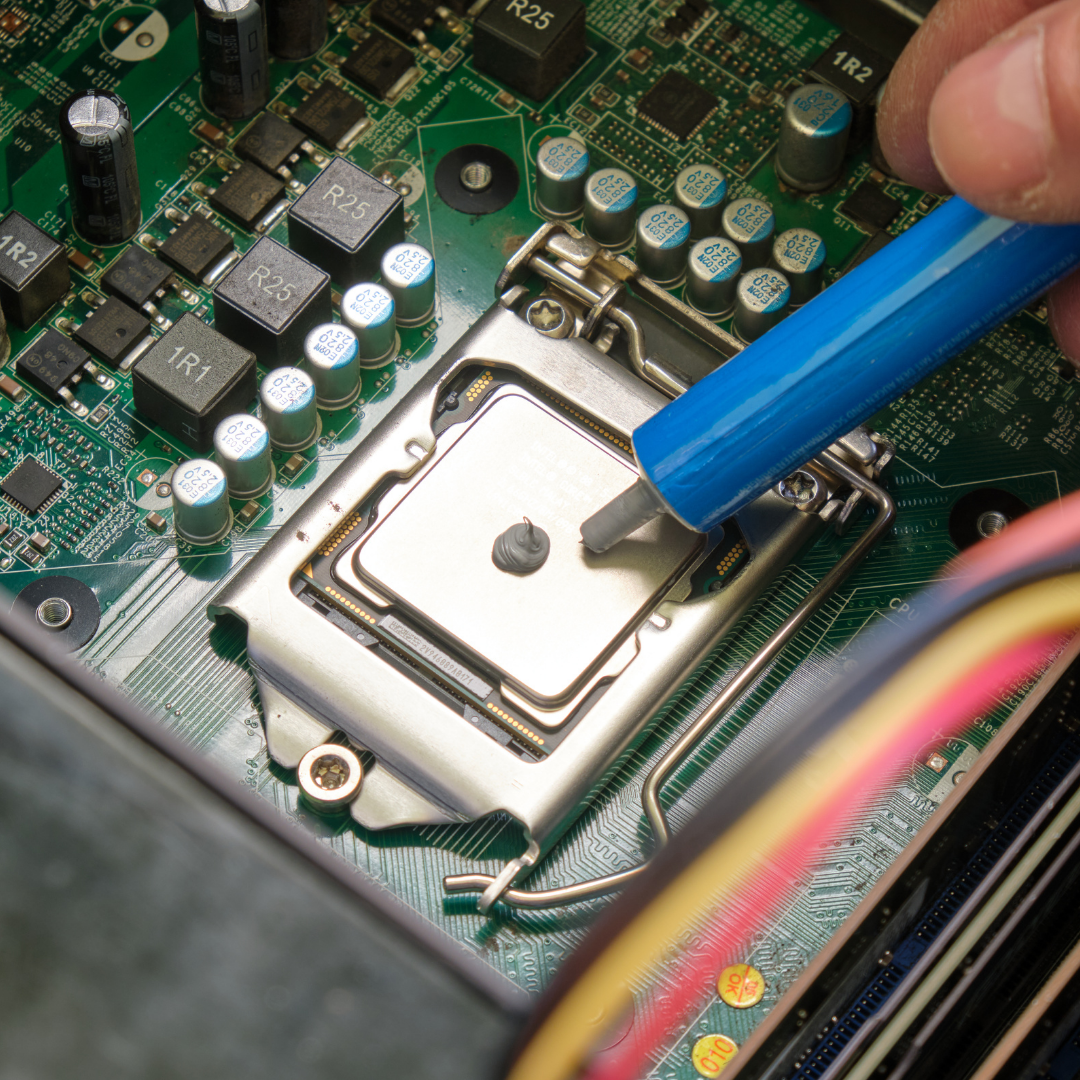 Close-up of a computer motherboard with a person's hand applying thermal compound to a central processing unit (CPU) using a blue applicator.