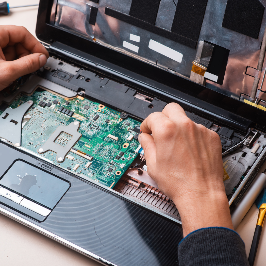 Close-up of hands repairing a laptop, with the laptop open and internal components visible.