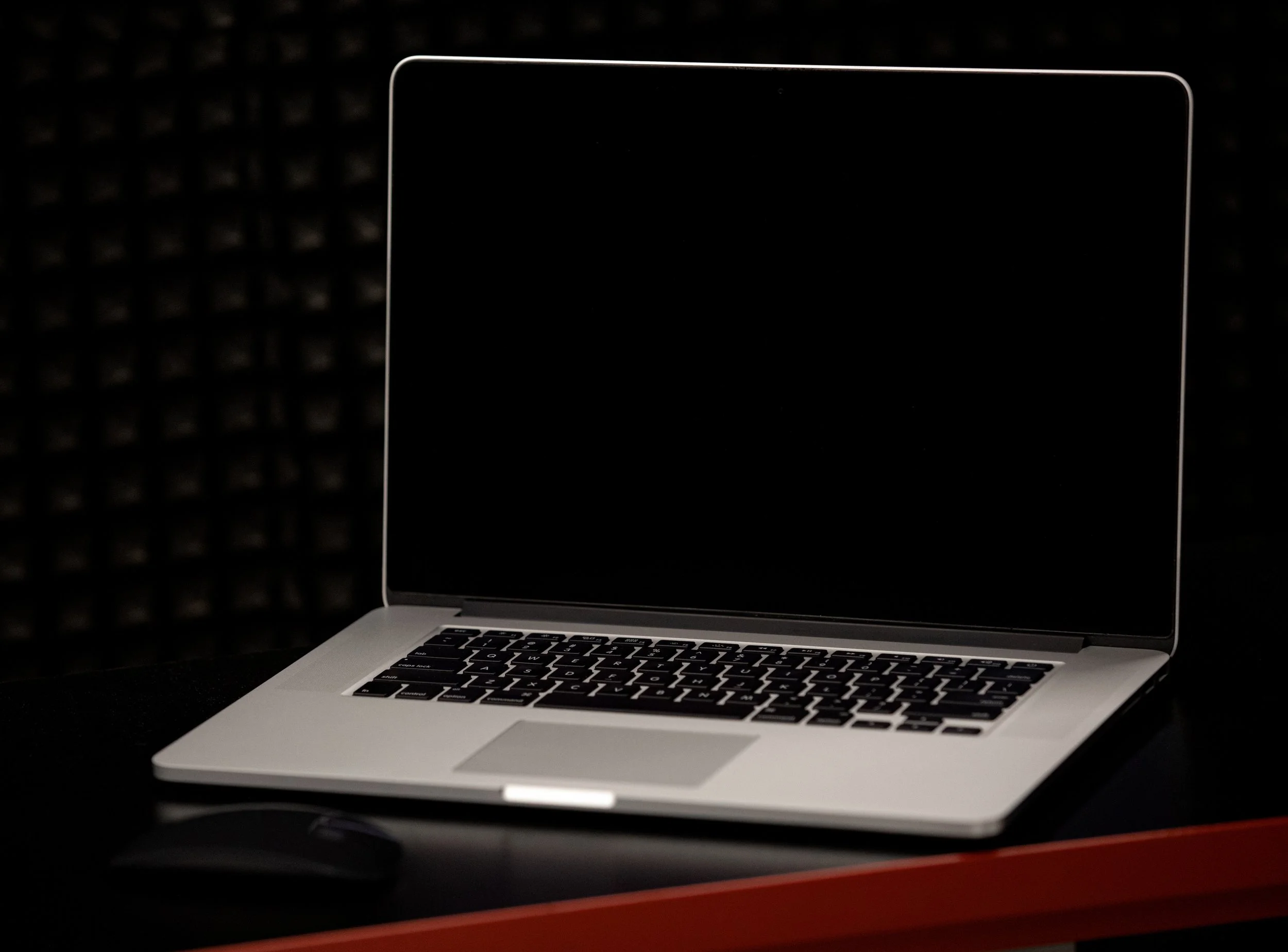 A silver laptop computer with black keyboard resting on a red surface against a black textured background.
