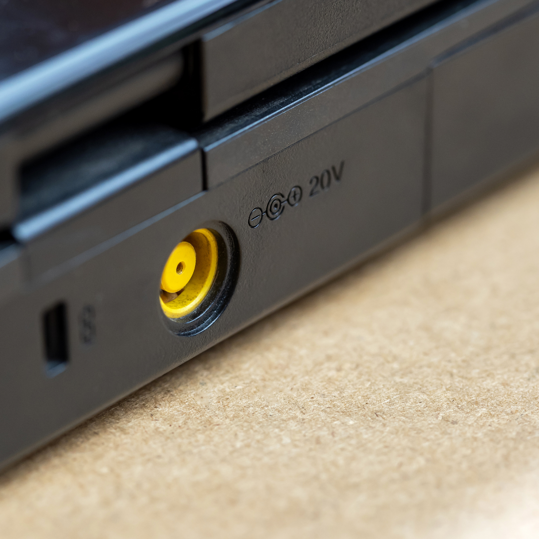 Close-up of a laptop's power port and voltage label, showing a round yellow power input socket and indicator markings for 20V.