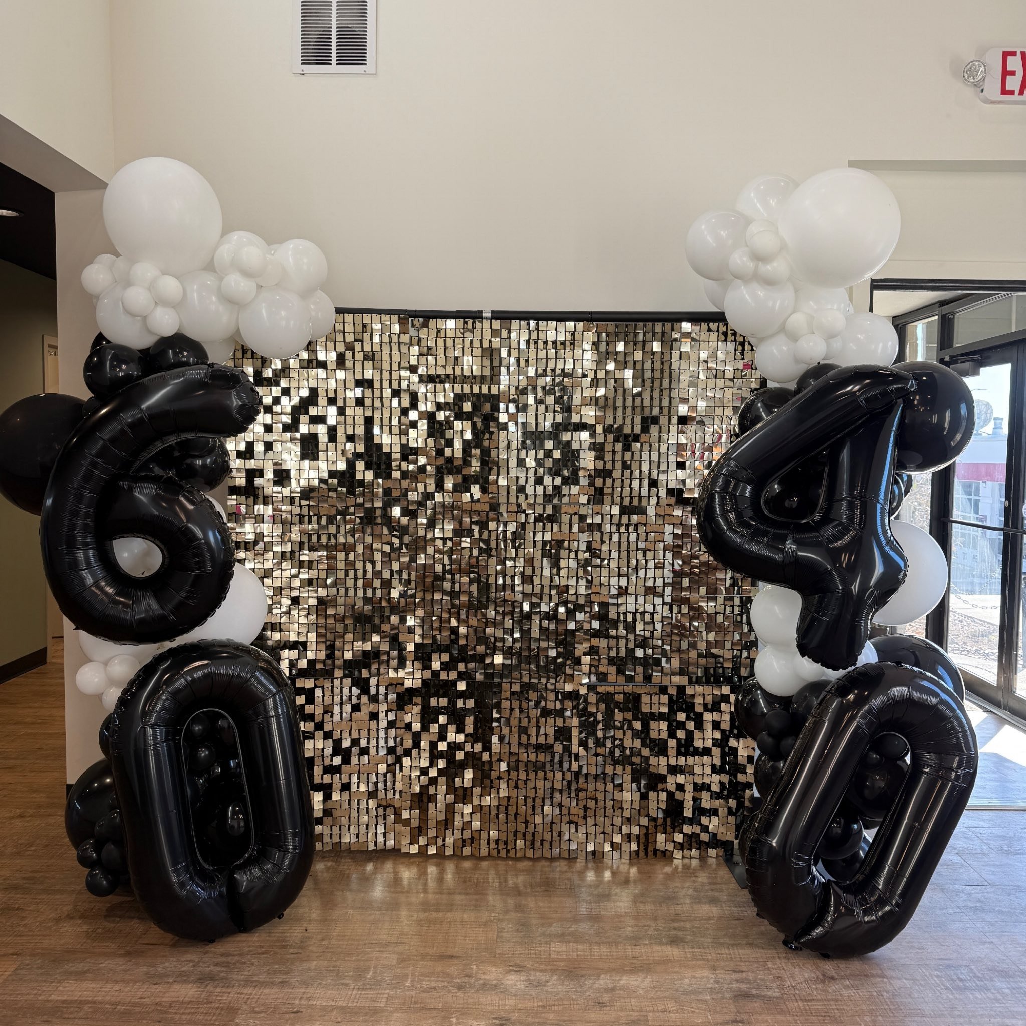 Decorative balloon arrangement featuring black and white balloons, with a shiny, reflective backdrop.