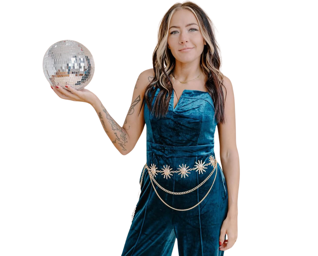 A young woman in a blue velvet jumpsuit holding a disco ball, standing against a black background.