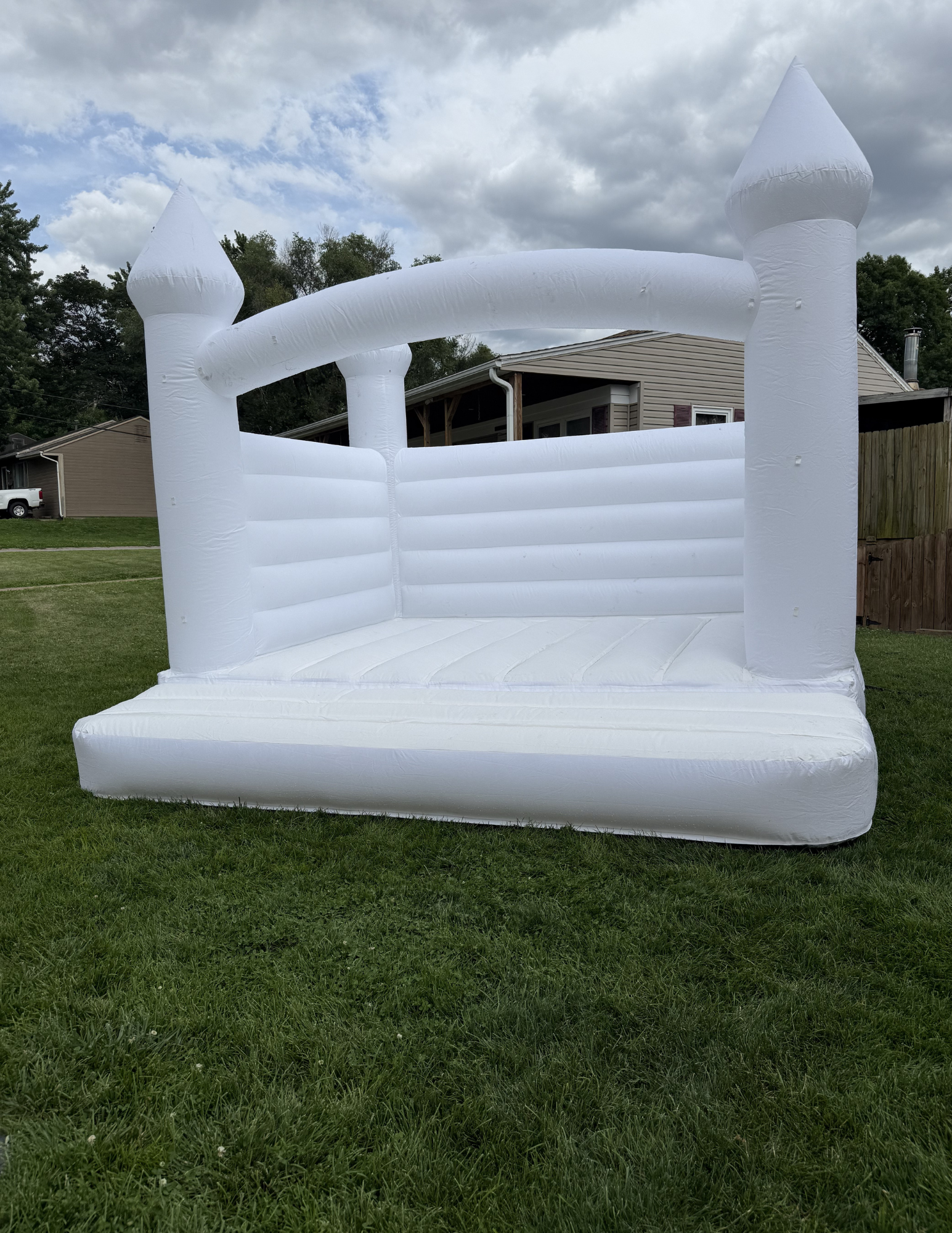 Inflatable white castle bounce house on a grassy yard, with a house and trees visible in the background under a partly cloudy sky.