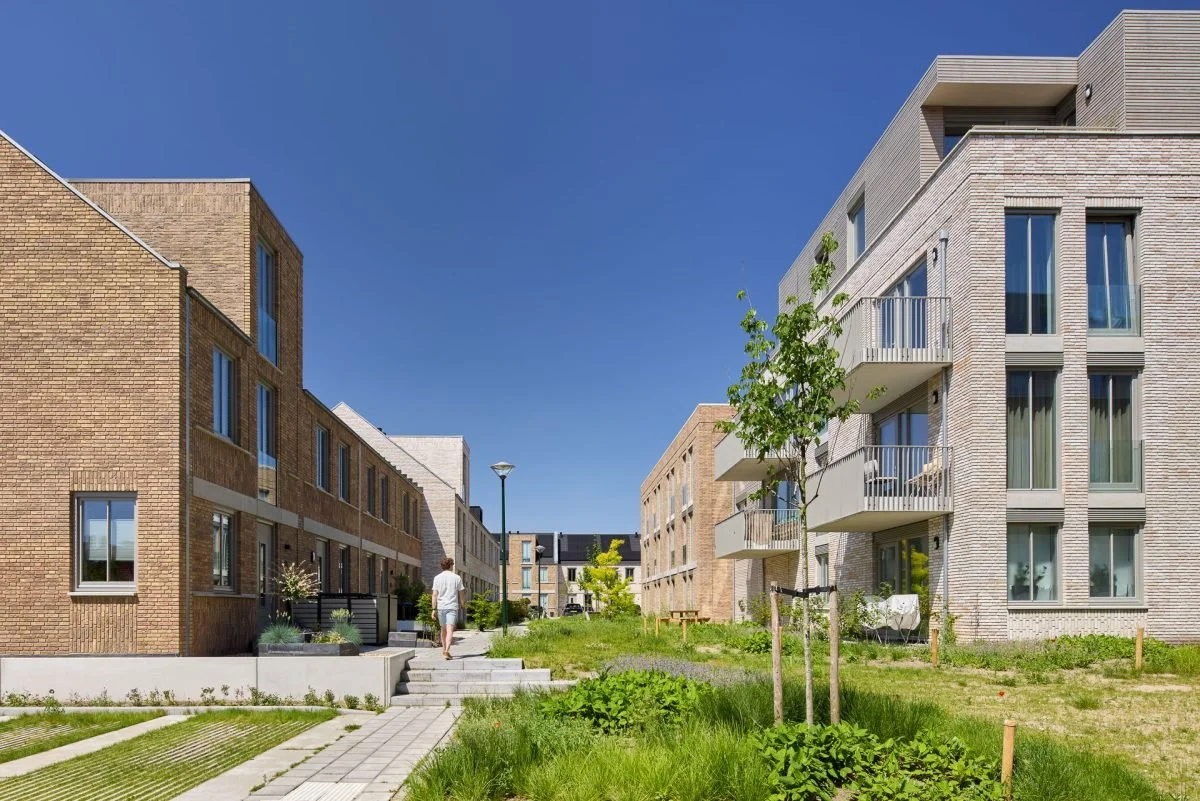 Moderne appartementencomplexen met groene tuin en wandelpad onder een blauwe hemel.