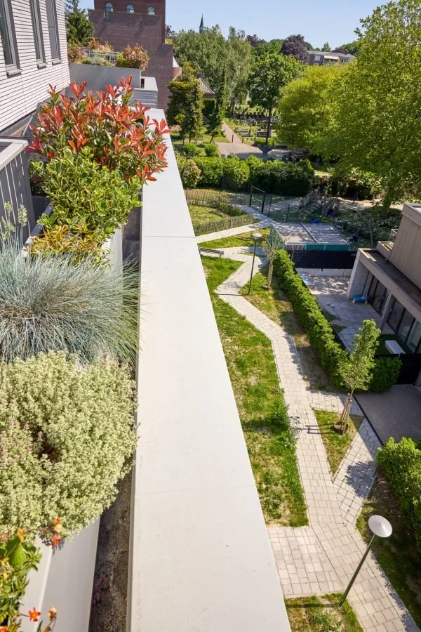Uitzicht over een groene tuin met wandelpaden, bomen en planten, gezien vanaf een balkon of terras op een hogere verdieping.