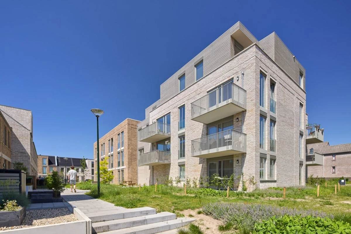 Moderne witte en beige appartementen met balkons, groene tuin en een helderblauwe lucht.