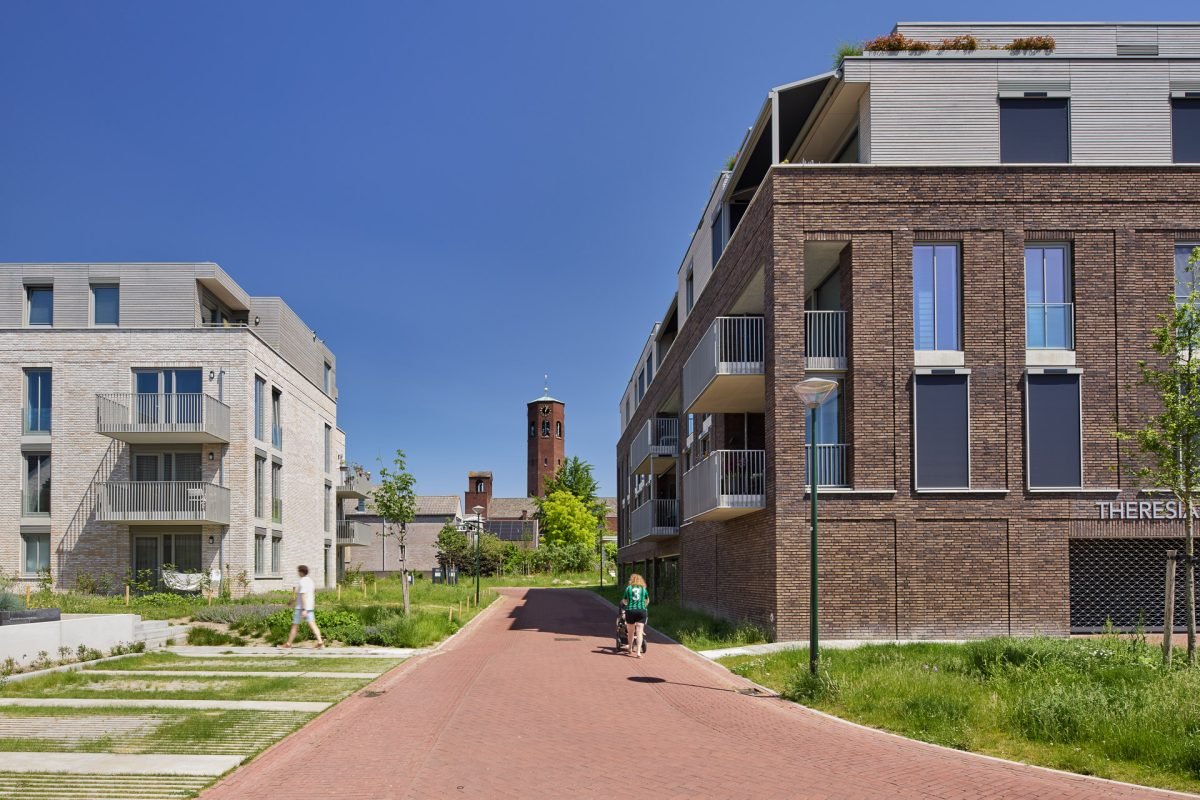 Moderne appartementen in een woonwijk met een fietspad en mensen die wandelen en fietsen, onder een blauwe hemel.