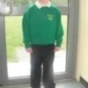 Young boy wearing a green hoodie and black pants standing in front of a glass door