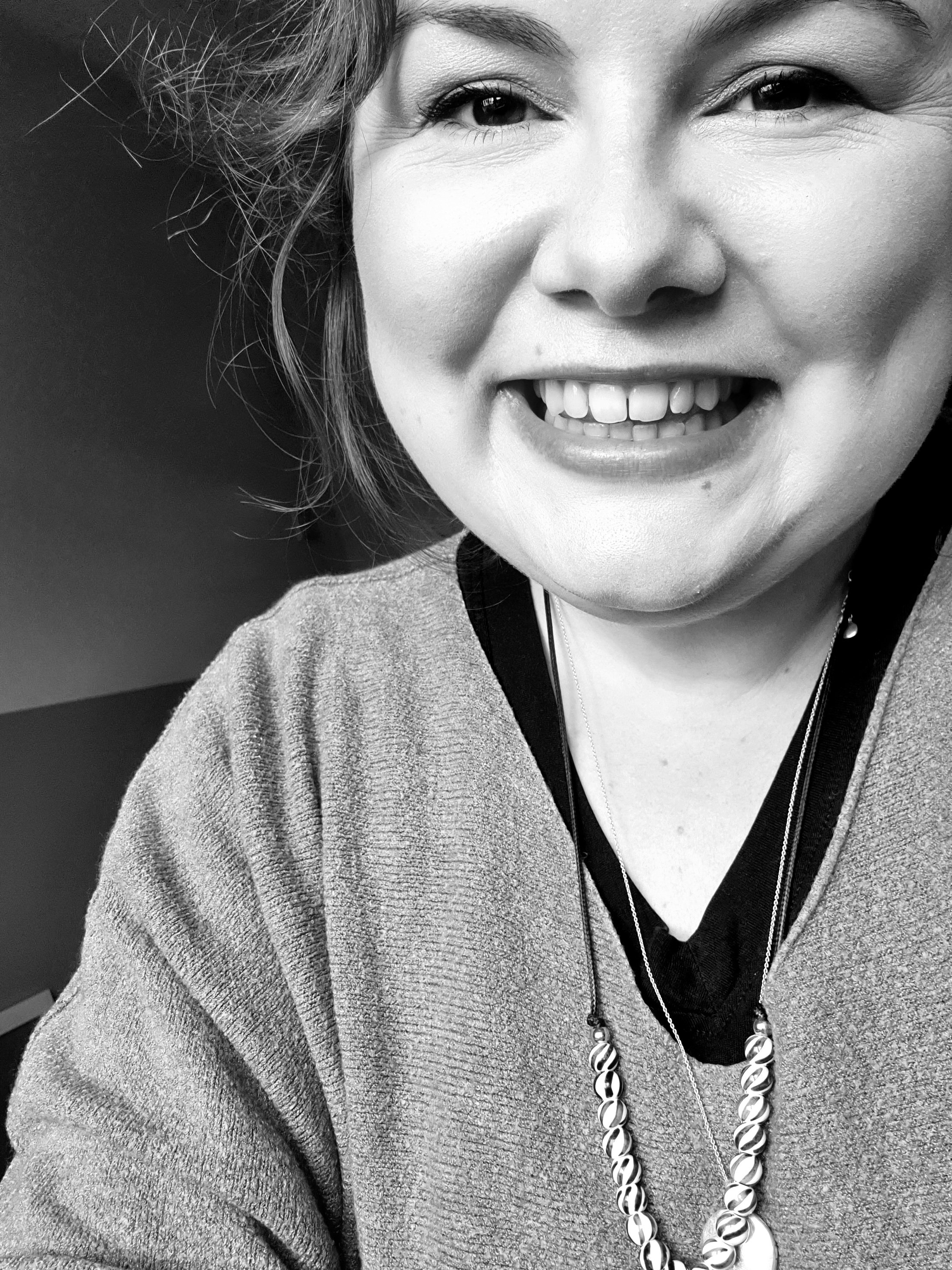 A black and white photo of the artist Alice Chapman smiling in her home studio in Cheltenham.