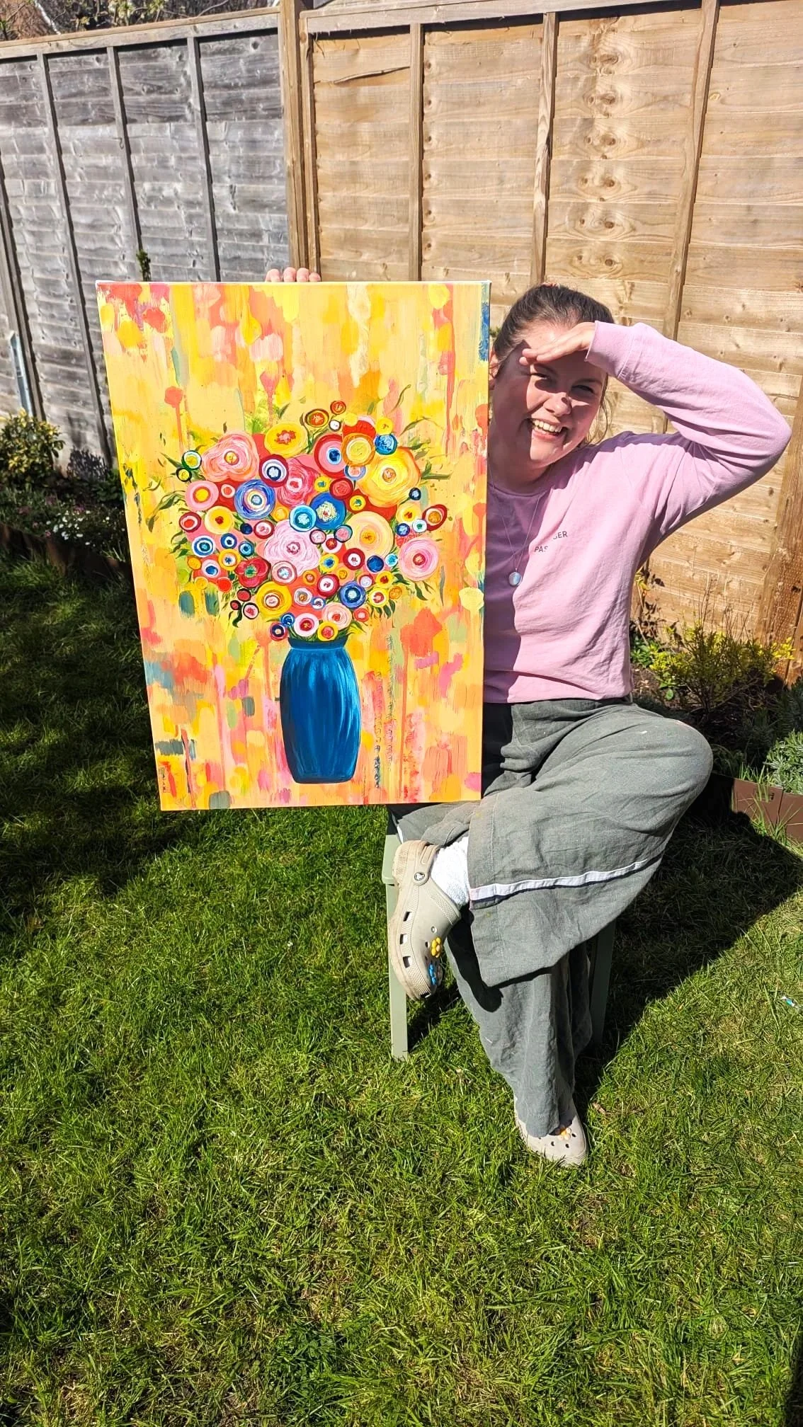 Artist Alice Chapman is sat in her garden proudly holding one of her most famous paintings 'Colour me happy', a vibrant floral painting that she sold at the 2026 Art in the Park exhibition.