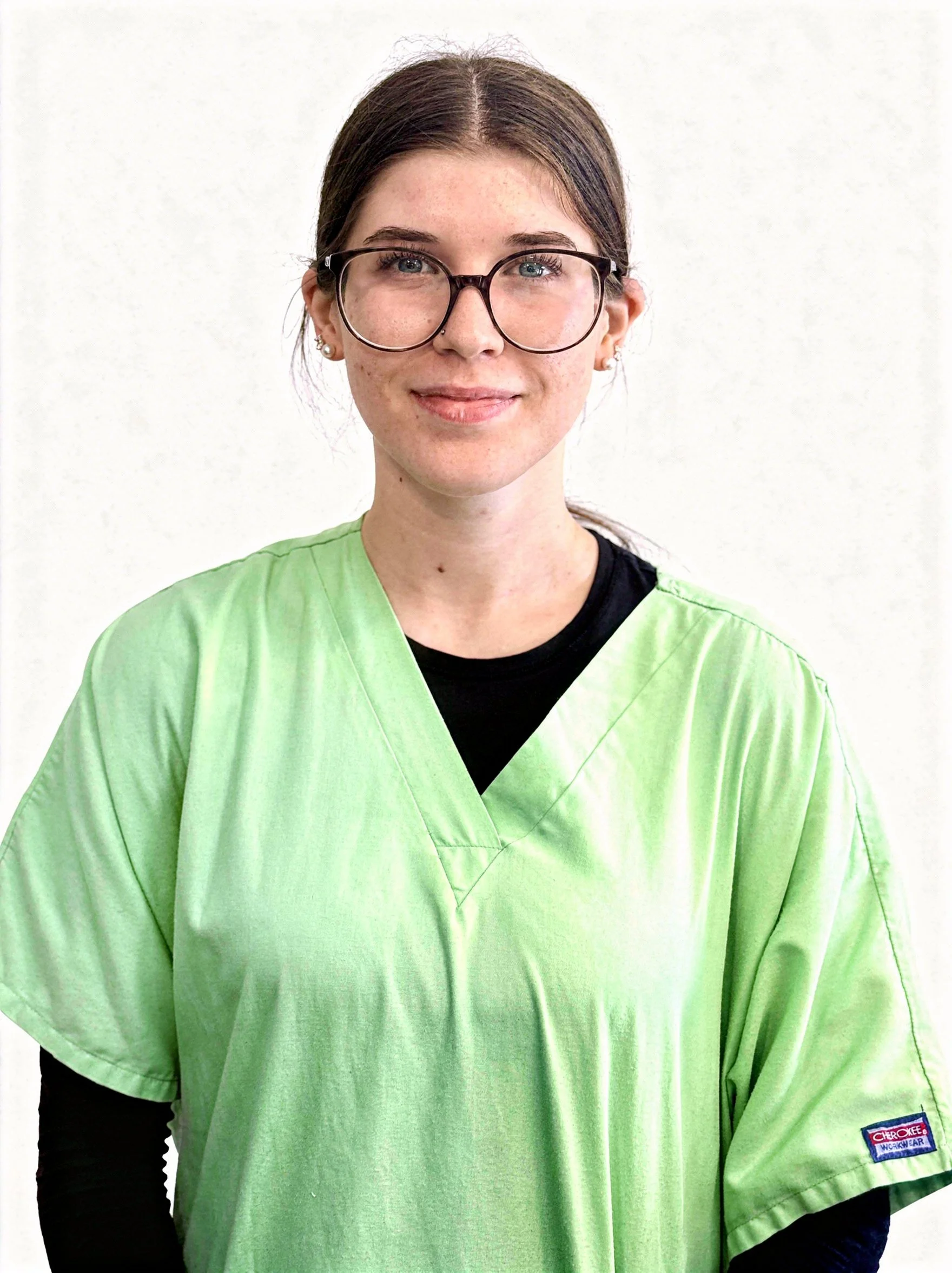 Young staff member in green medical scrubs, smiling, white background.