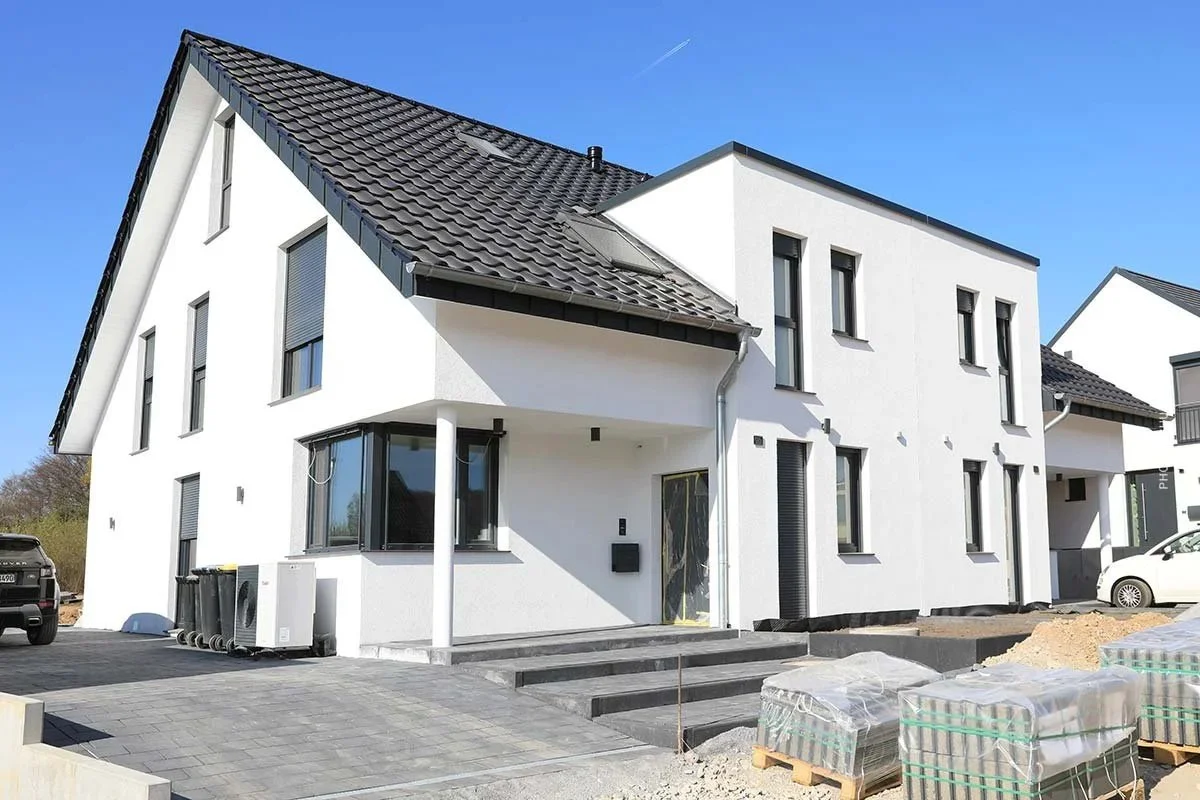 Ein modernes, weißes Wohnhaus mit dunklem Dach unter einem klaren blauen Himmel.