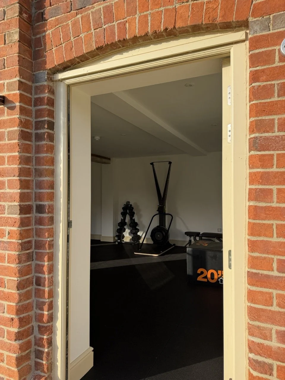 View through a partially open door into a home gym with exercise equipment, including a rowing machine, dumbbells, and a plyometric box.