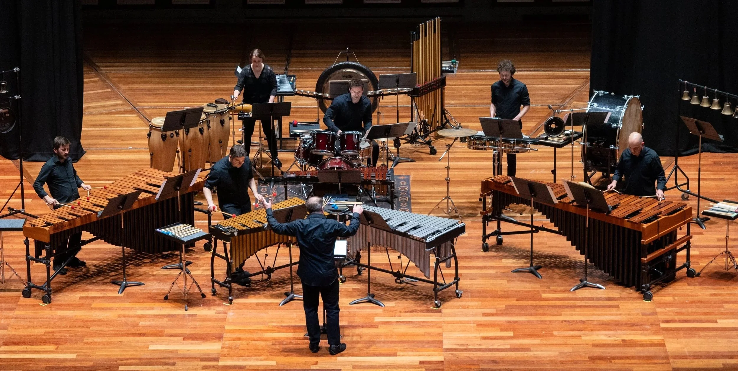Five members of the Colin Currie Group performing on stage with various percussion instruments, including marimbas, vibraphone, xylophones, drums, and chimes.
