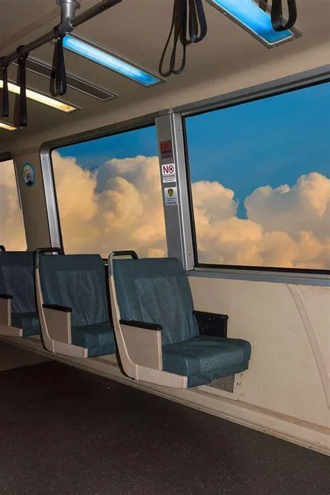 Inside an aircraft, empty blue seats facing a window viewing a sky with fluffy clouds.