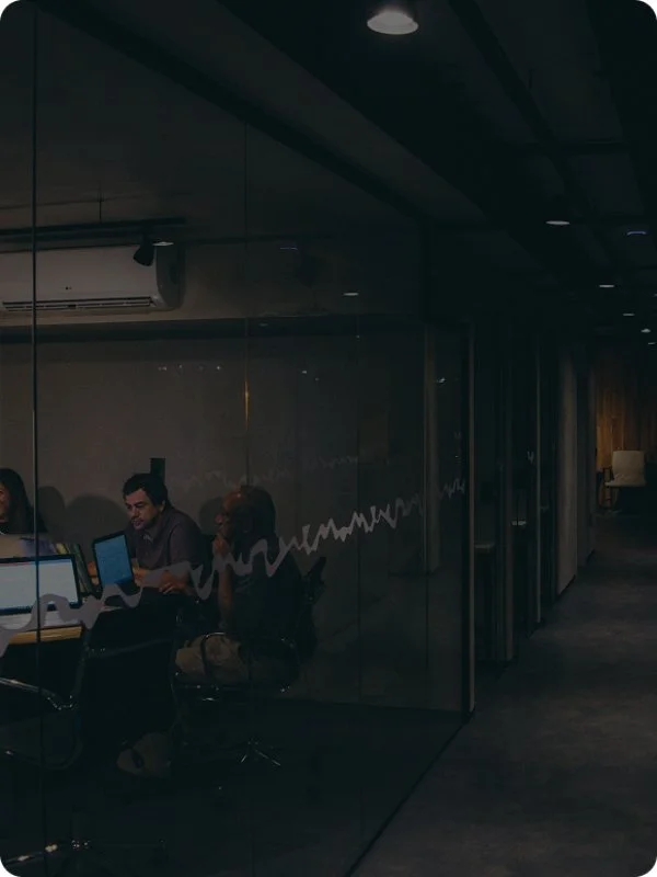 People sitting at a table in a modern office conference room with glass walls and laptops.