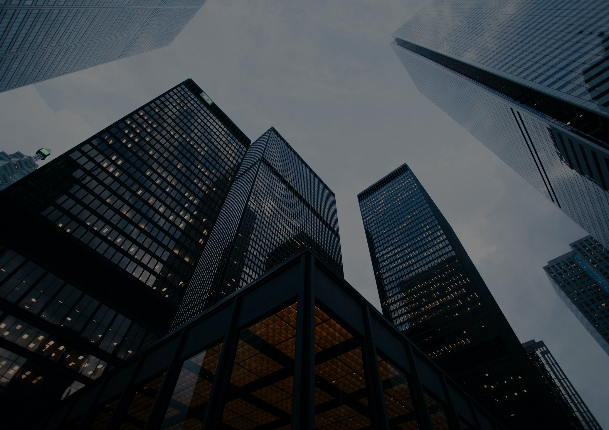 Looking up at tall glass skyscrapers in a city, with reflections and a cloudy sky.