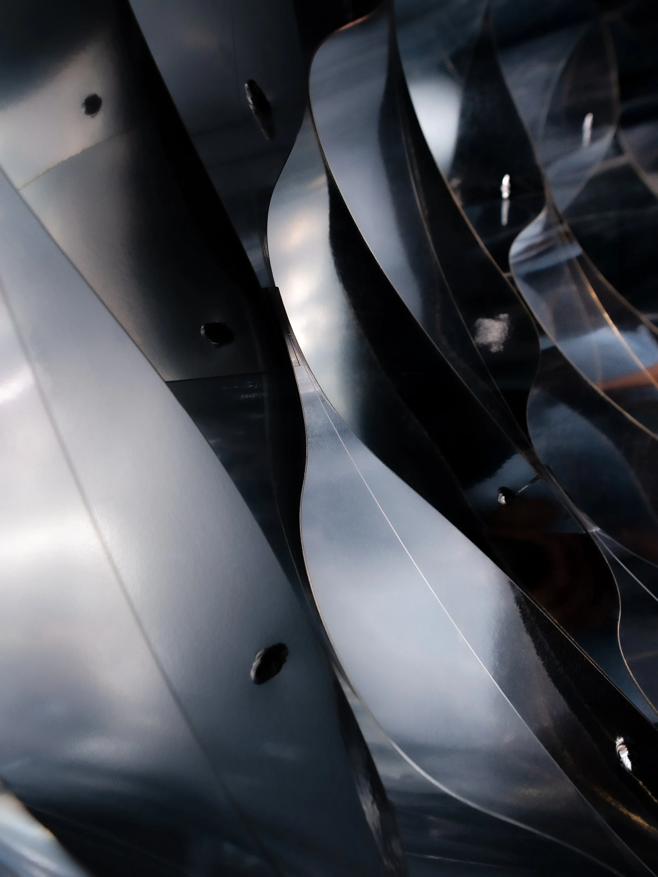 Close-up view of metallic, curved structures with shiny, reflective surfaces, possibly parts of art installation or modern architectural design.