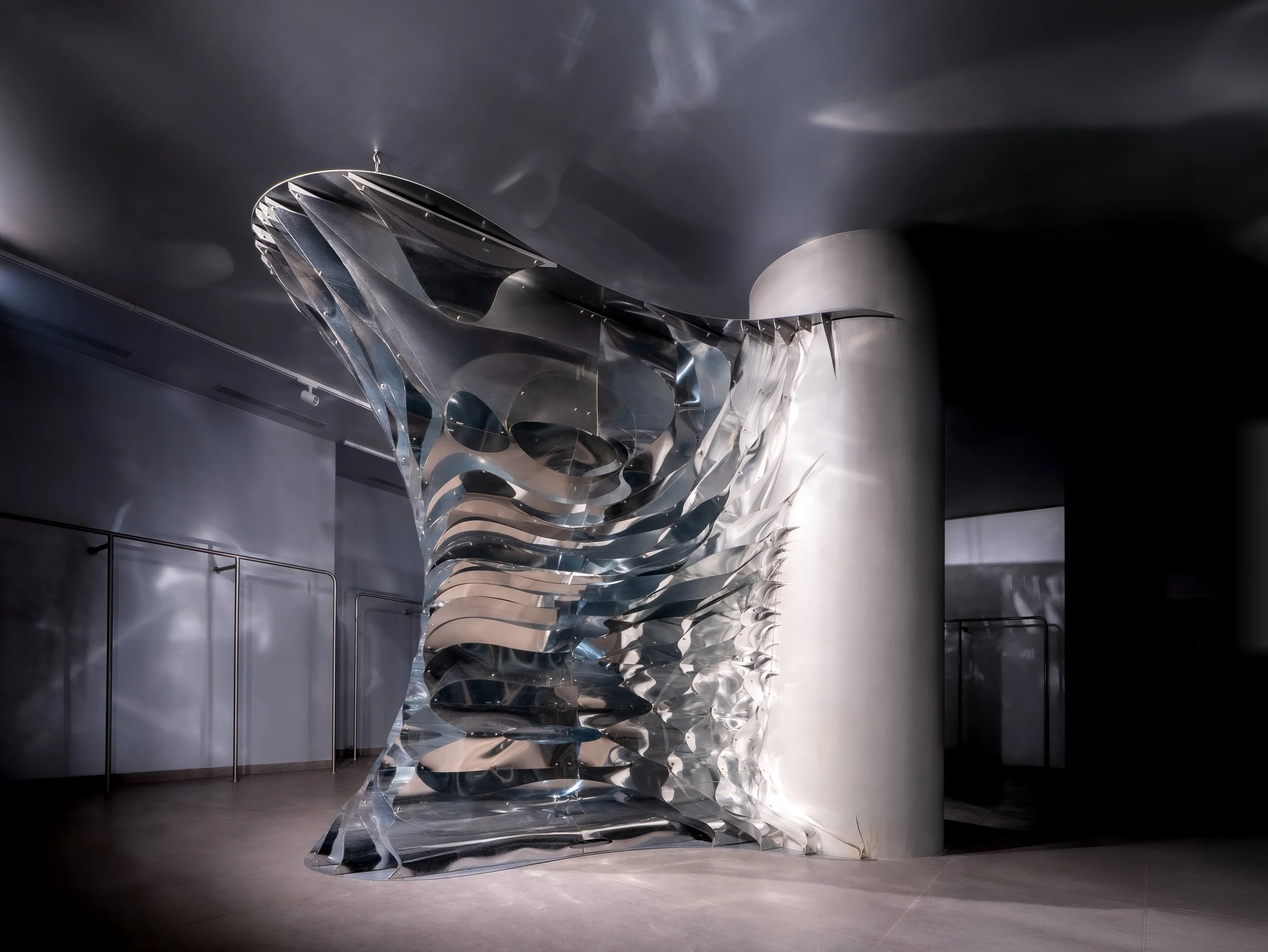 Modern art sculpture made of shiny, curved metal sheets on display in a gallery.