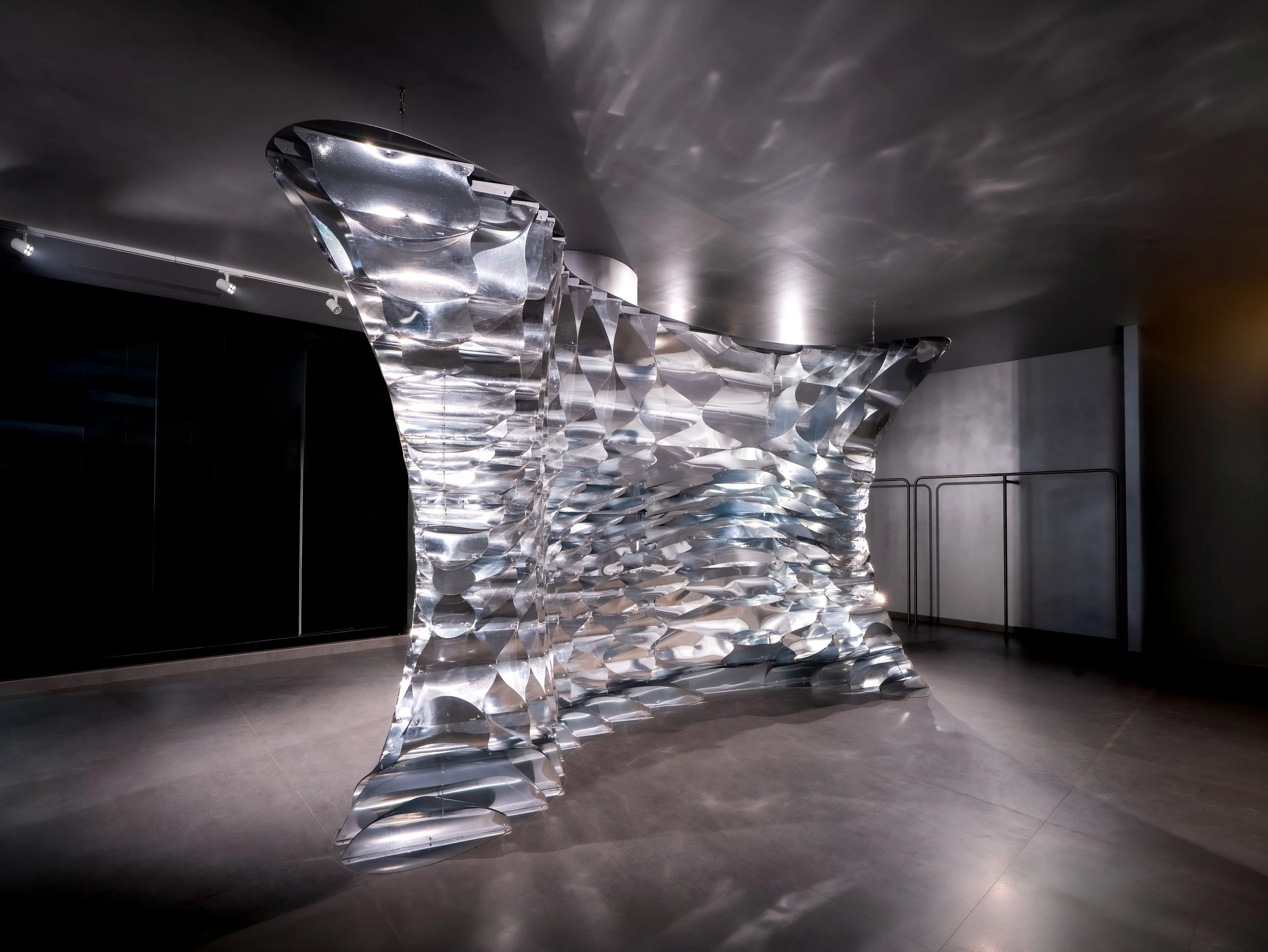 Modern art installation made of interconnected shiny metallic discs forming a flowing, wave-like sculpture inside a gallery space.