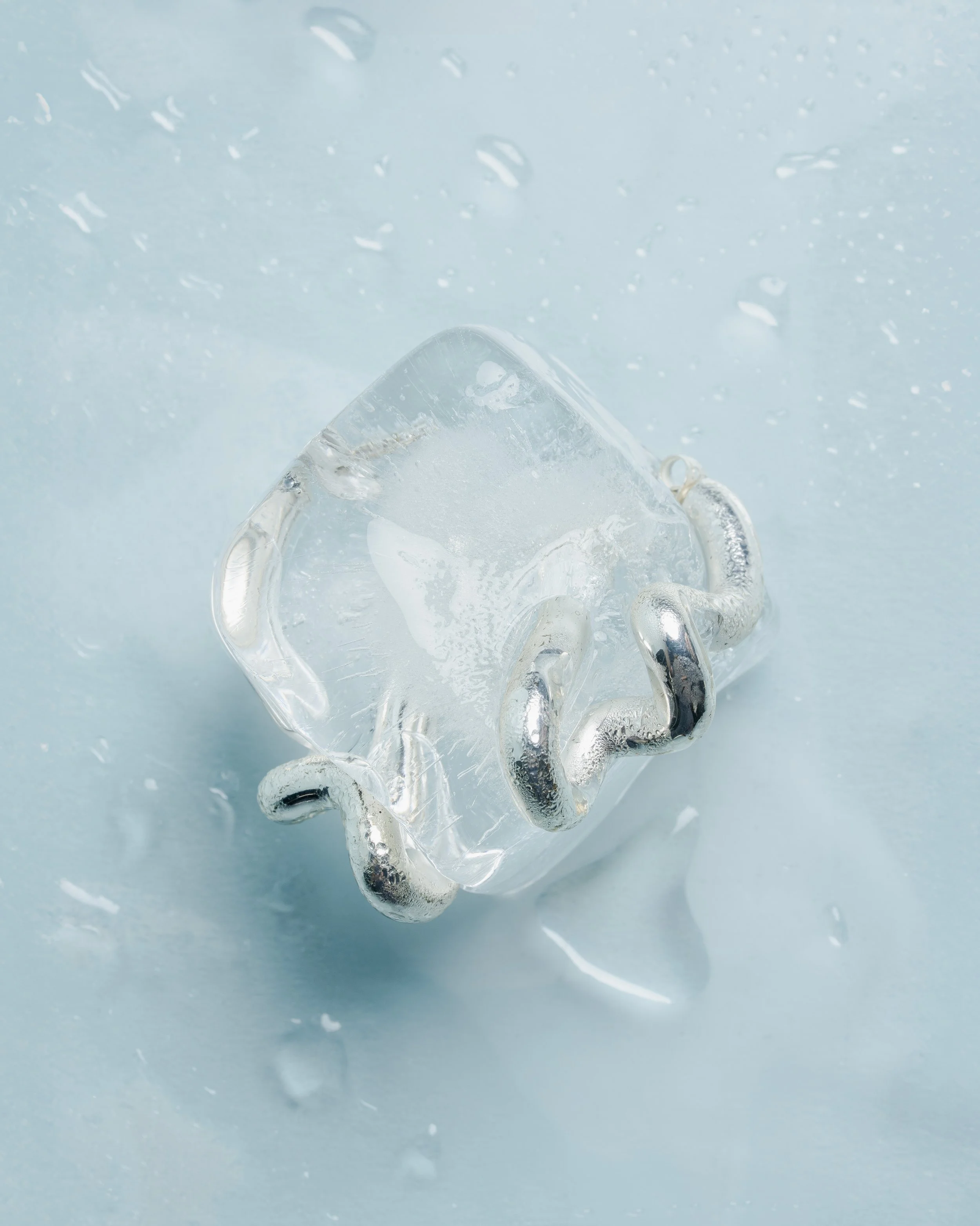 Close-up of a clear glass heart-shaped ornament on a light blue surface, with water droplets and ice visible.