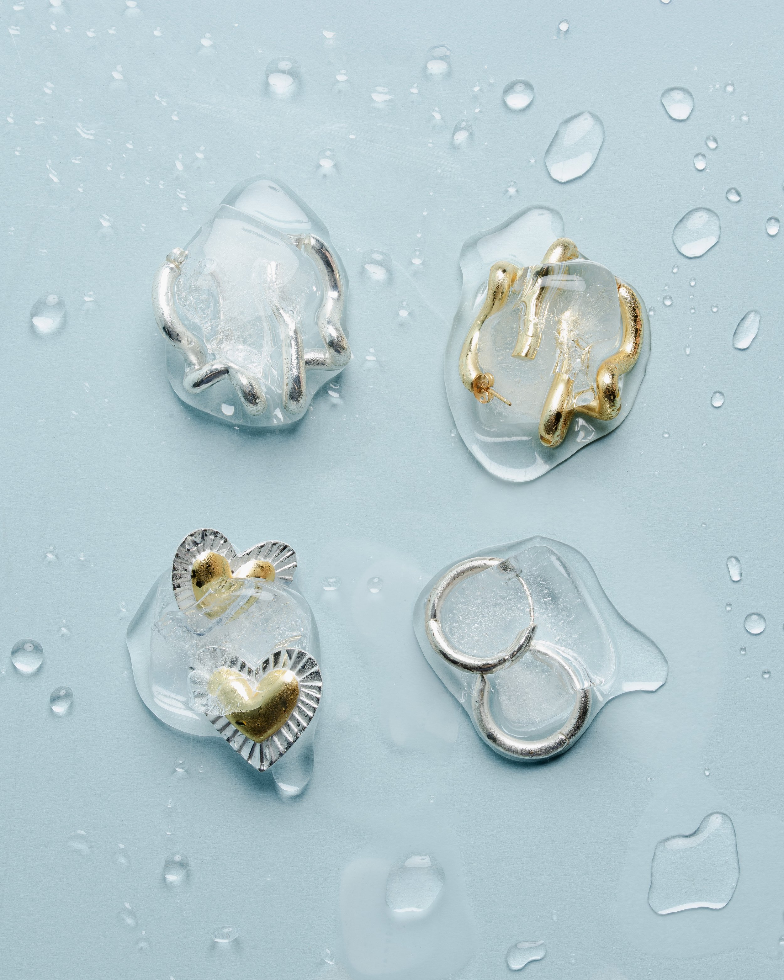 Close-up of broken and melted jewelry pieces on a wet, light blue surface with water droplets.