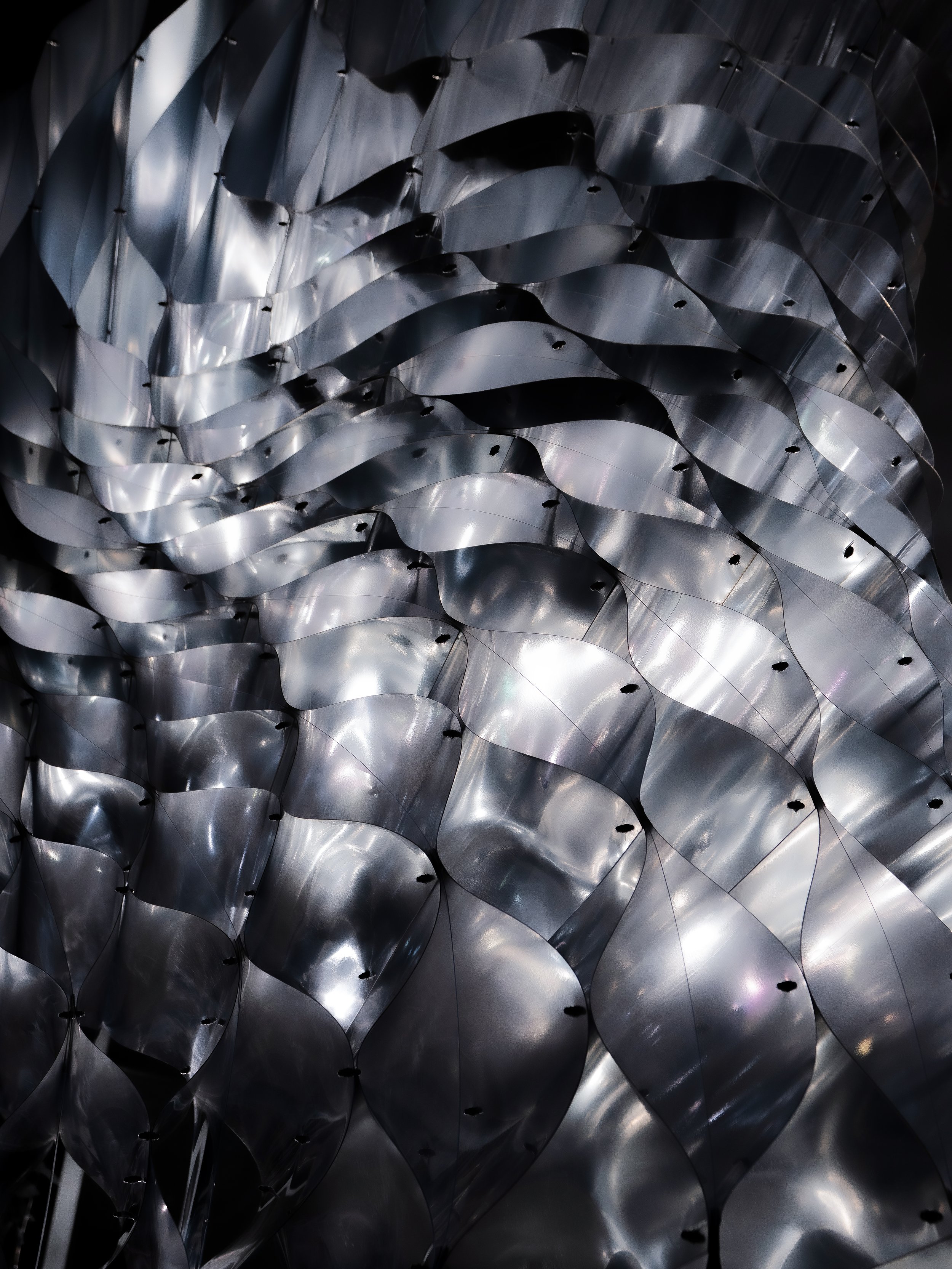 Close-up of a metallic sculpture with overlapping, curved, shiny silver ribbons arranged in a flowing pattern.