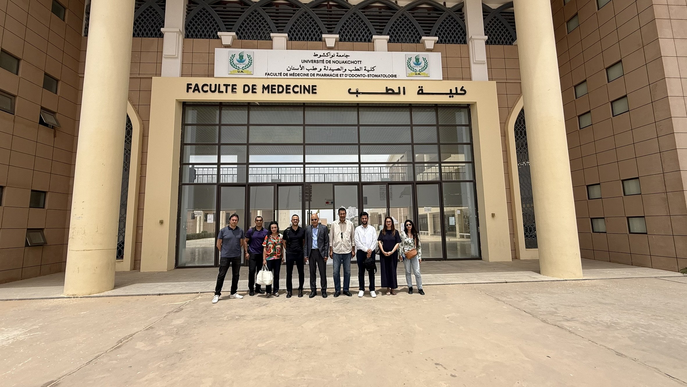 Groupe de personnes posant devant l'entrée de la faculté de médecine à l'université de Nouakchott.