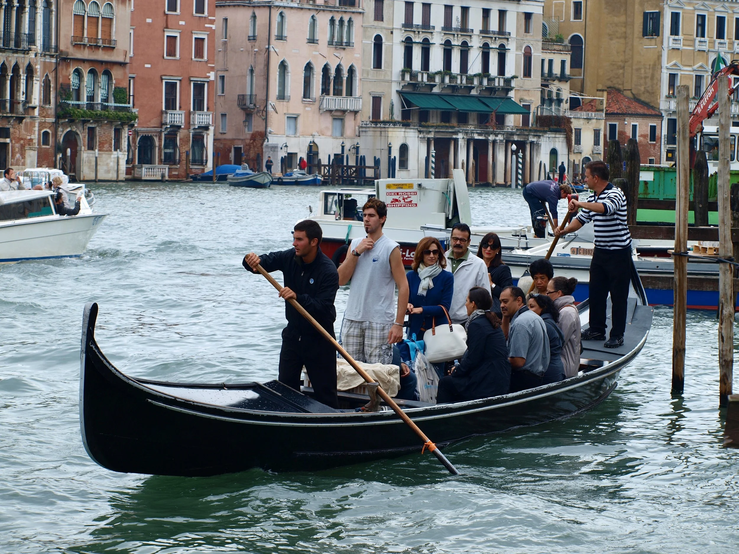 Des touristes naviguant en gondole sur une canal à Venise, avec des bâtiments historiques colorés en arrière-plan.