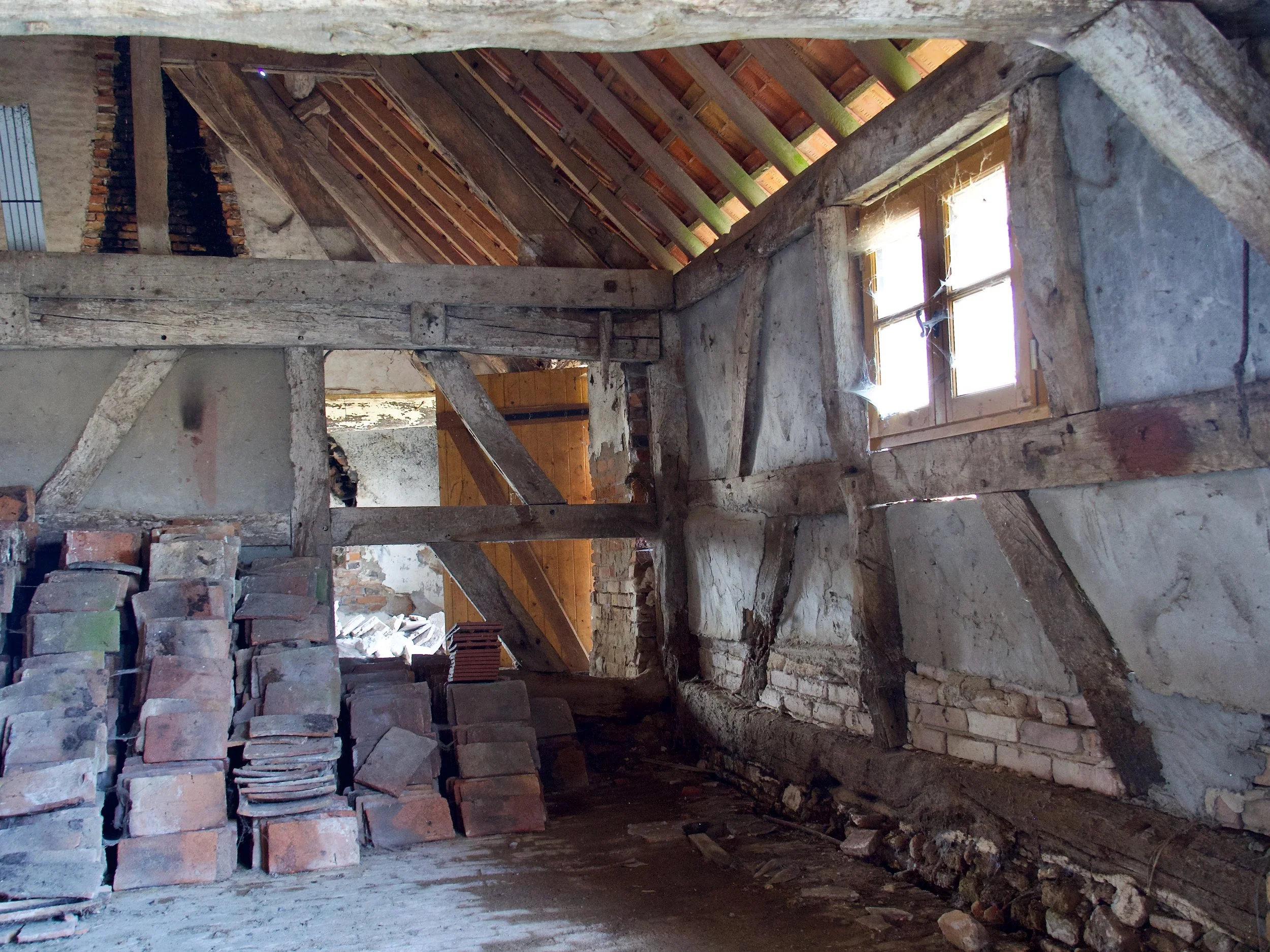 Intérieur d'une maison en rénovation avec des murs en pierre et un toit en bois non fini, avec des fenêtres laissant entrer la lumière.