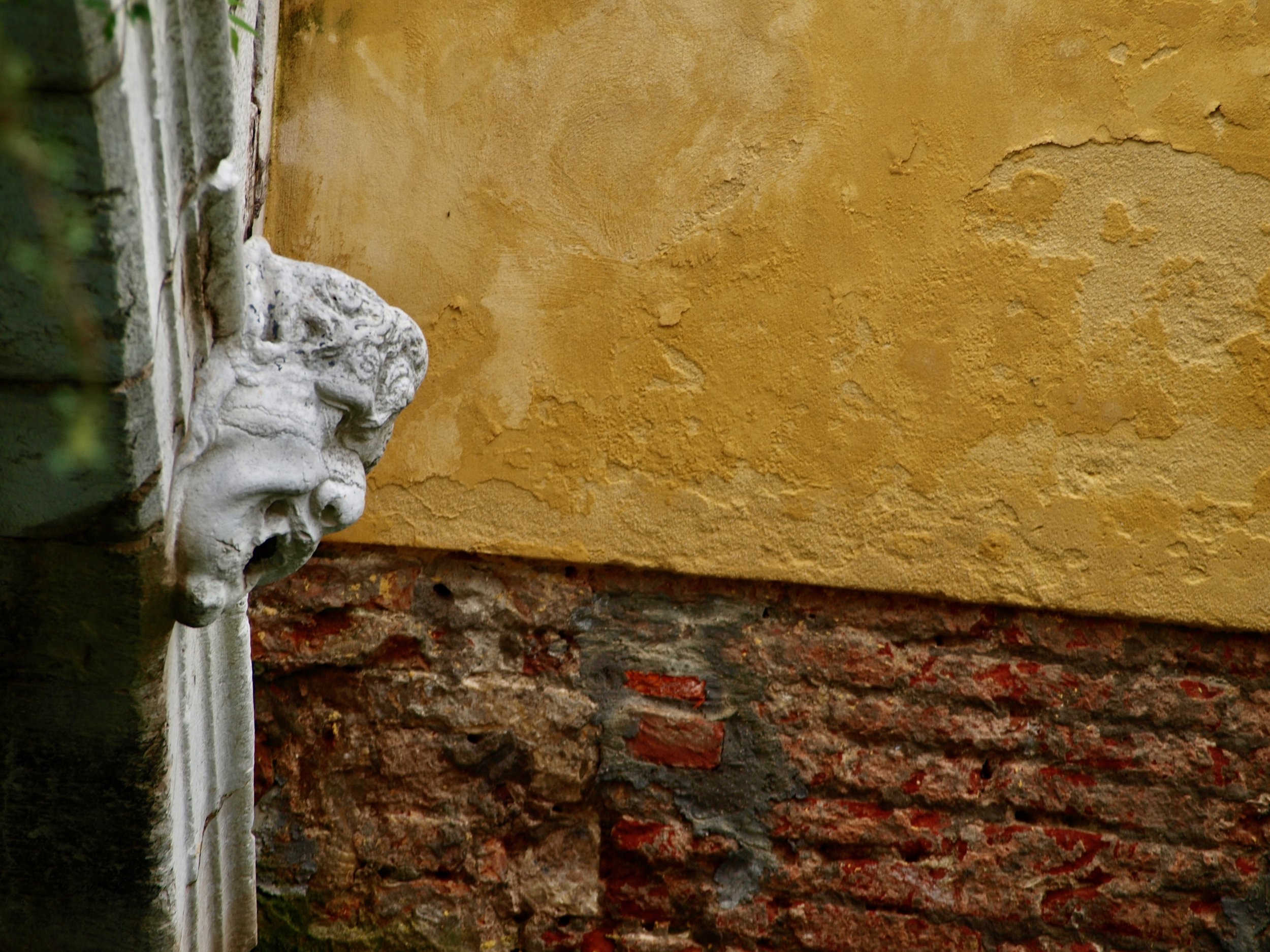 Une statue en pierre d'une tête humaine de profil, fixée à un mur en pierre avec un fond de mur jaune.