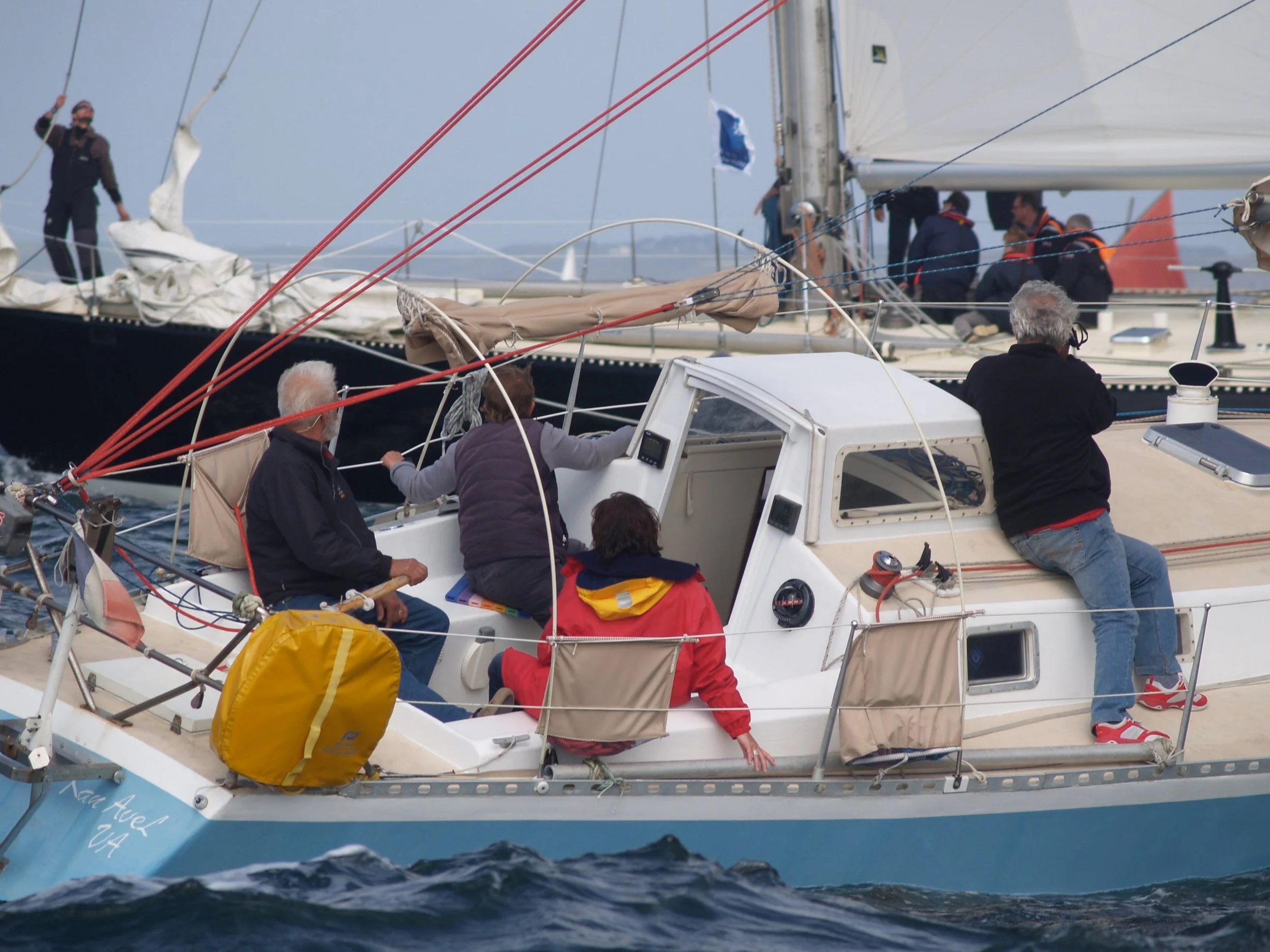 Une groupe de personnes sur un voilier occupé à la navigation en mer, avec certains ajustant les cordages et d'autres observant, dans un ciel légèrement nuageux.