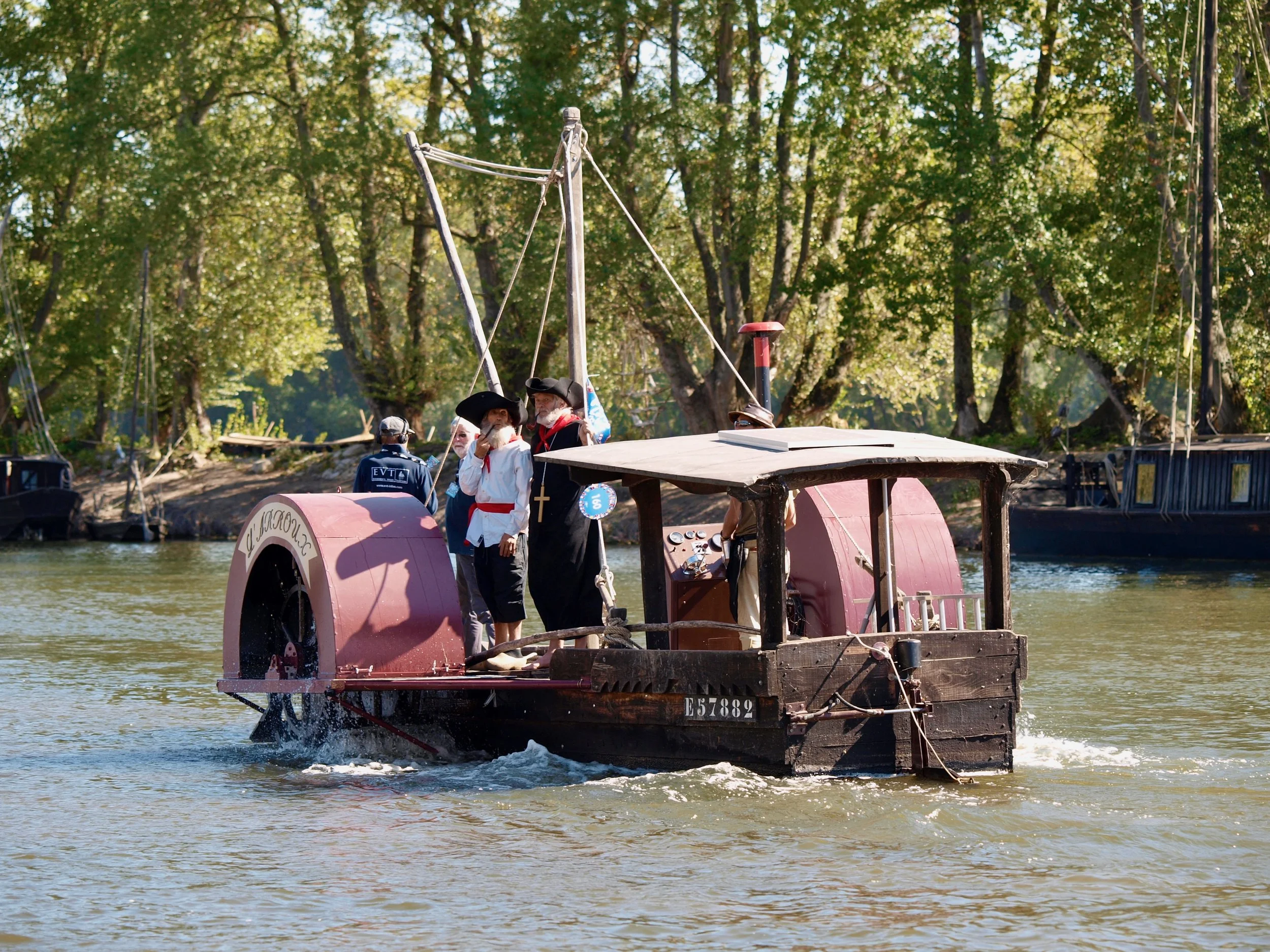 Bateau à vapeur avec des personnes habillées en costume d'époque naviguant sur la rivière dans un environnement boisé.