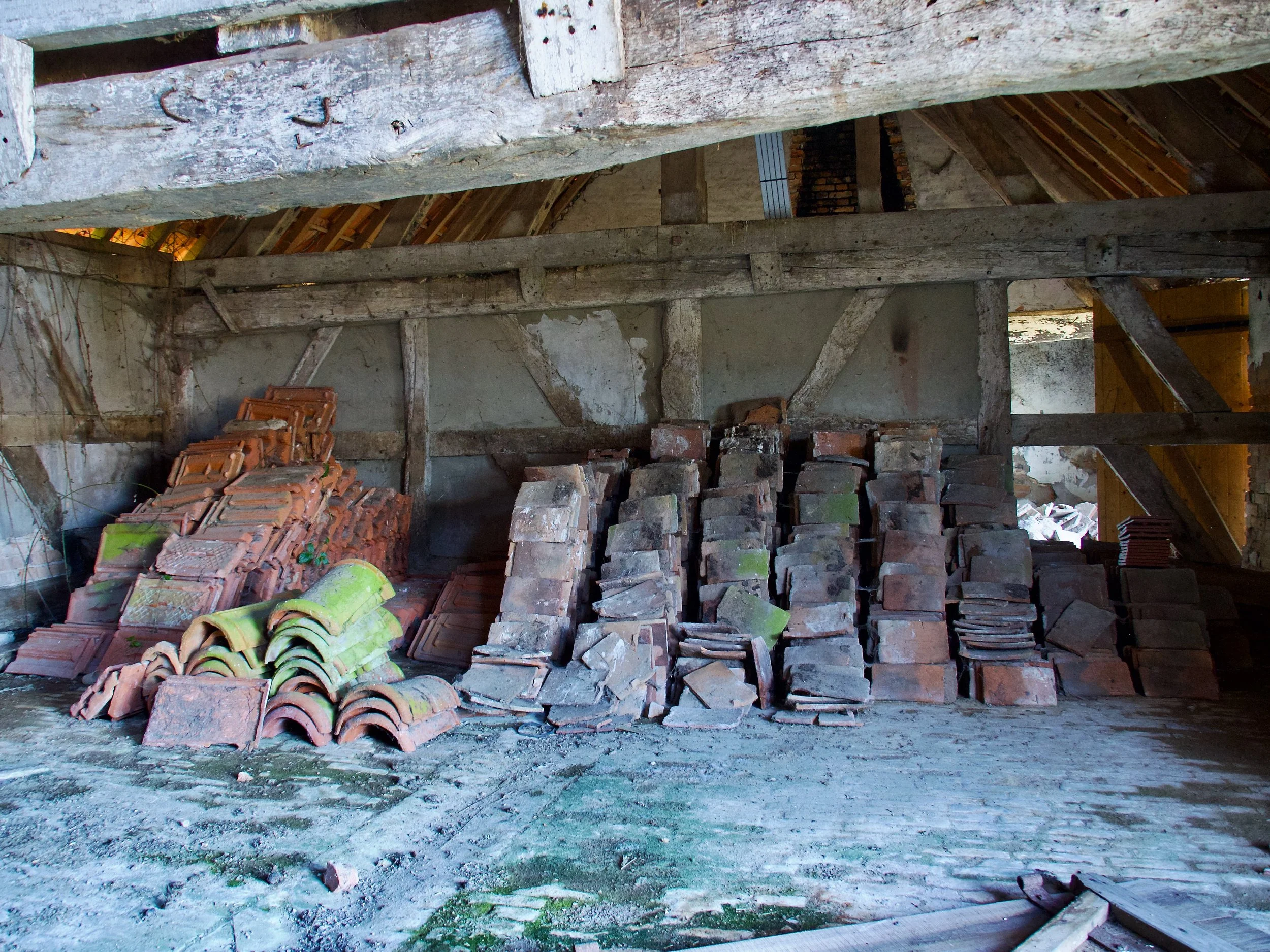 Intérieur d'un bâtiment en cours de construction avec des piles de briques en terre cuite, un mur en brique, et un plafond en bois non fini.