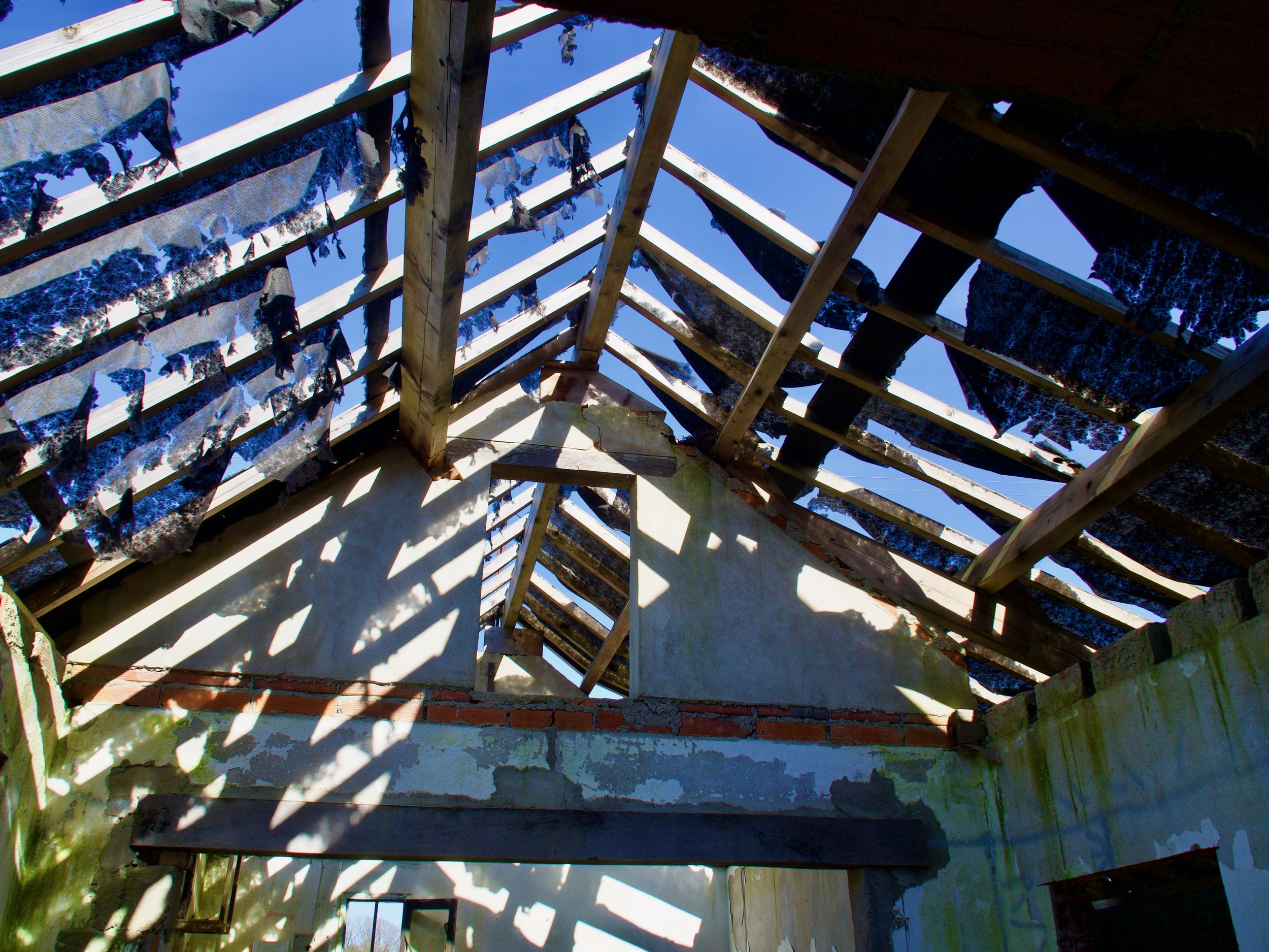 Structure en bois avec des tissus suspendus entre les poutres, un ciel bleu visible à travers le toit ouvert.