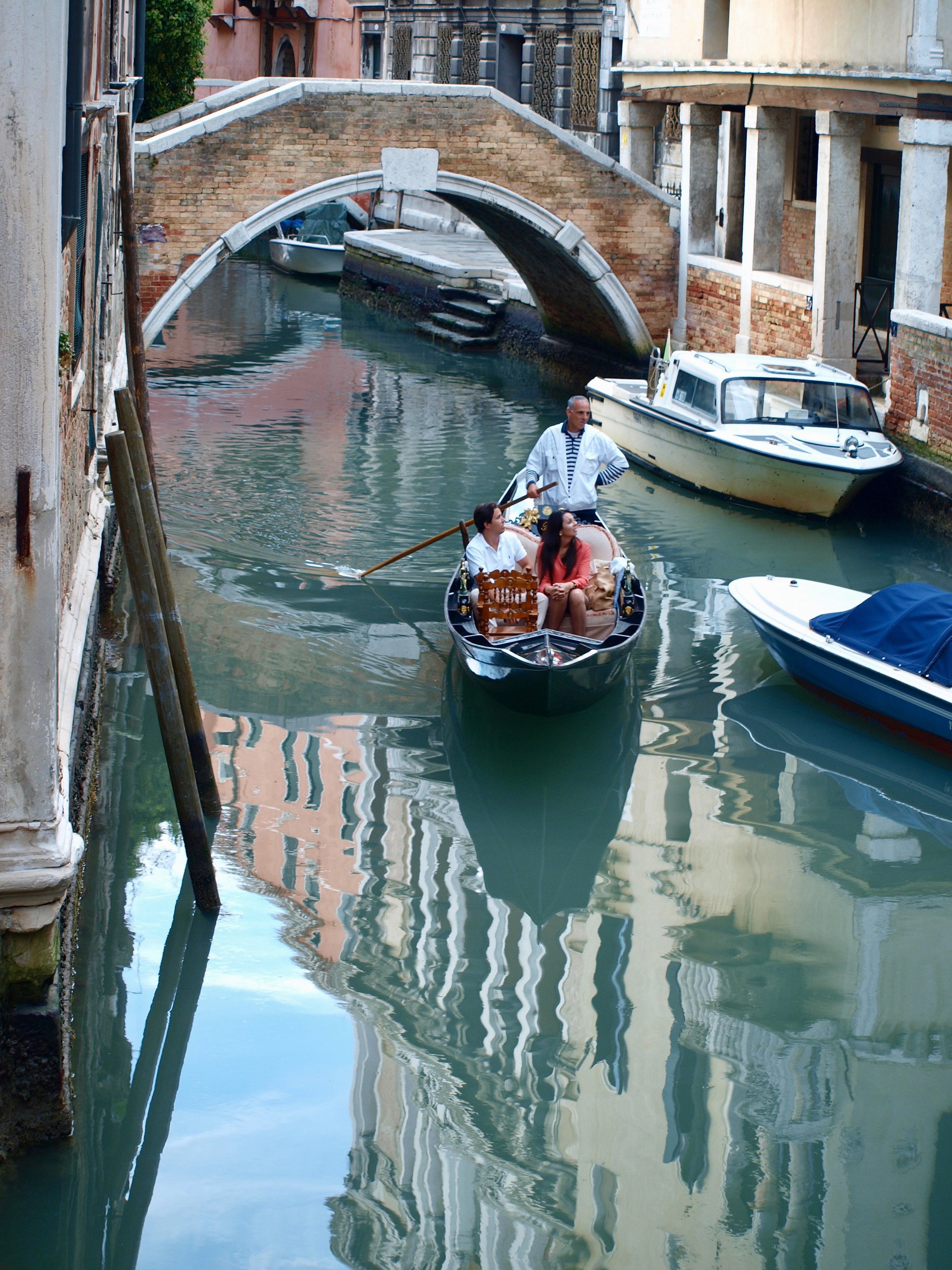 Une gondole avec deux touristes et un gondolier naviguant dans un canal de Venise, entouré de bâtiments anciens en brique.