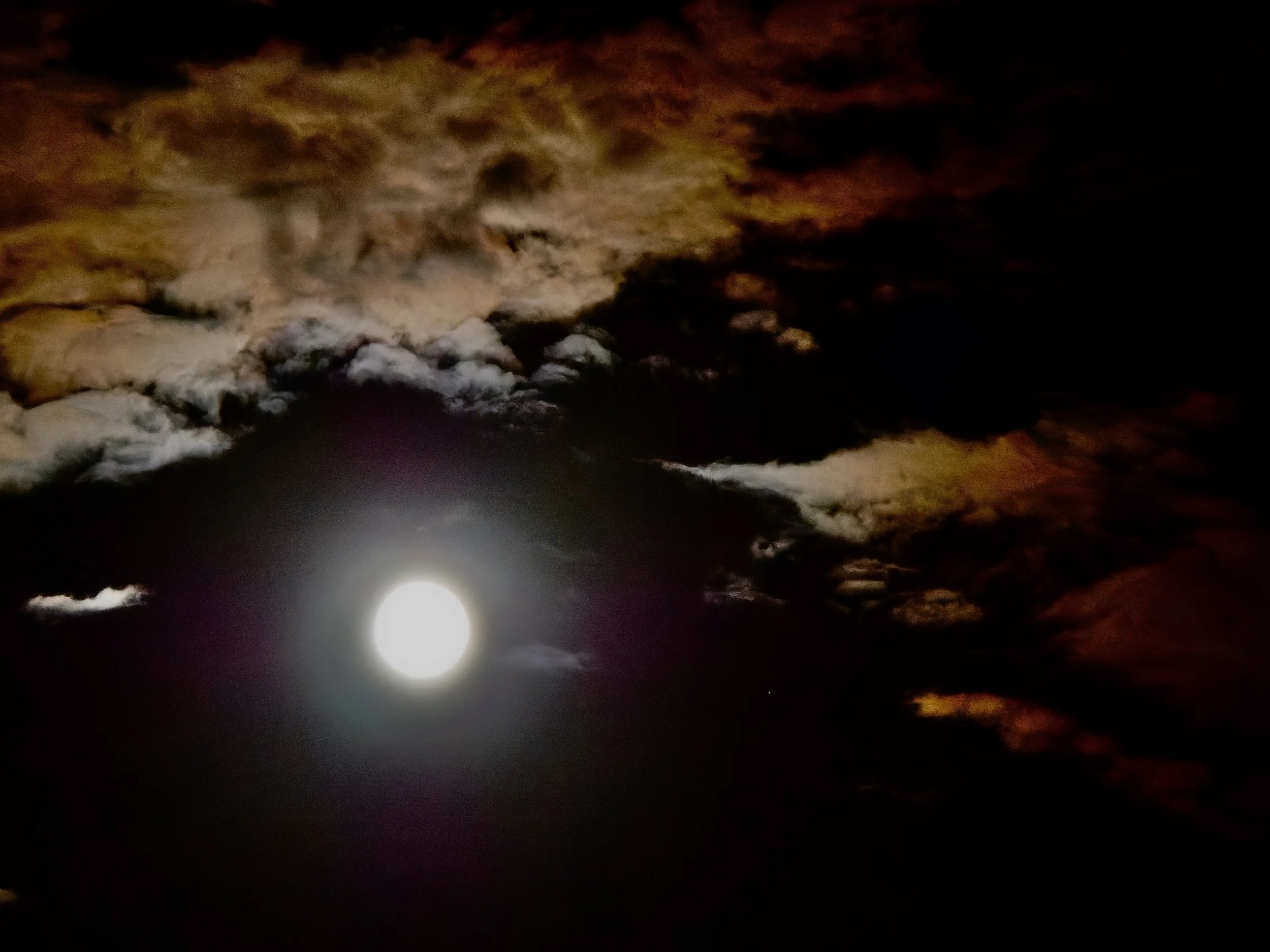 Lune brillante dans un ciel nuageux avec des nuages de couleur orange et marron.