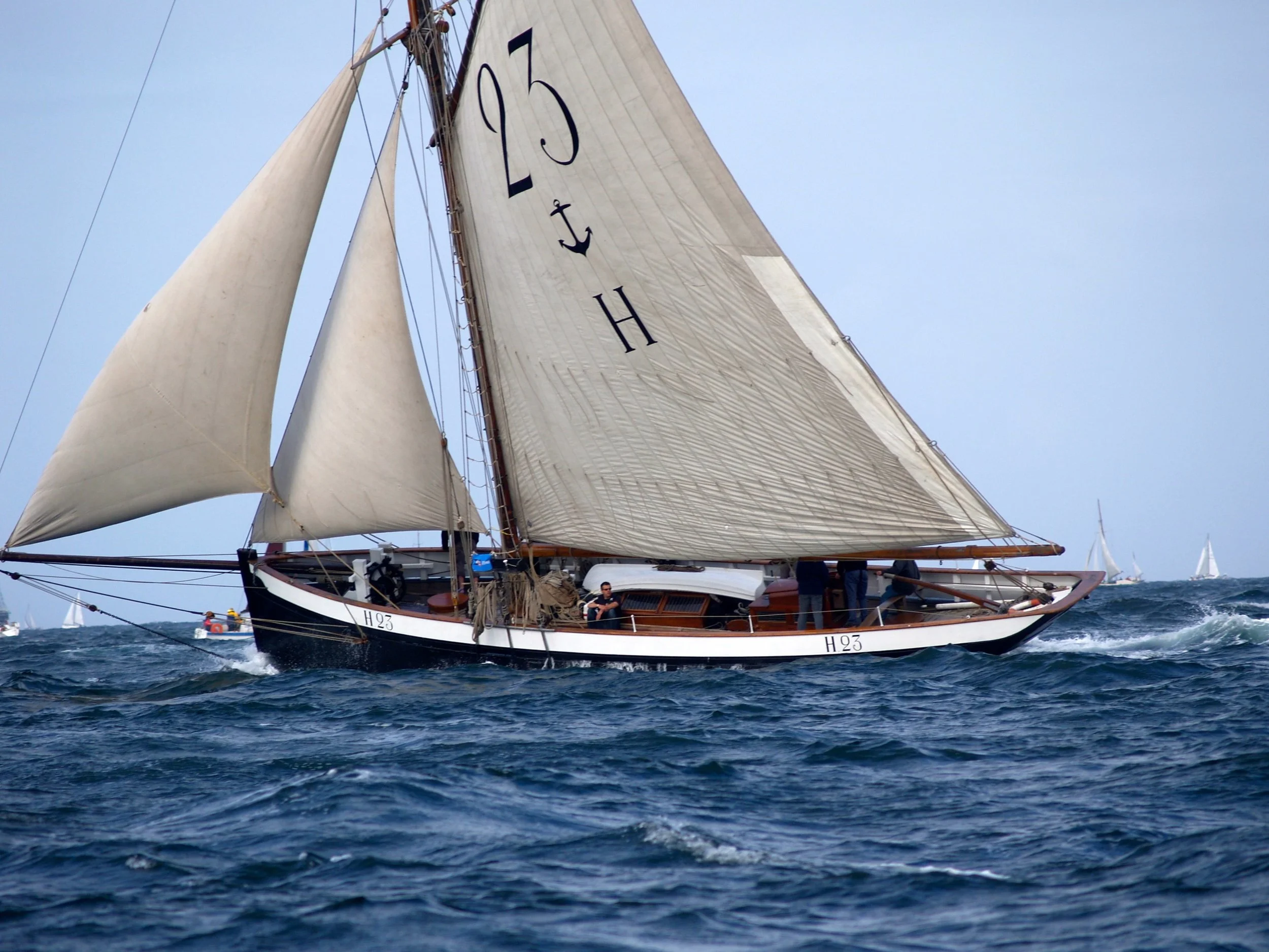Un voilier navigue sur la mer avec plusieurs mâts et voiles déployées, sous un ciel clair.