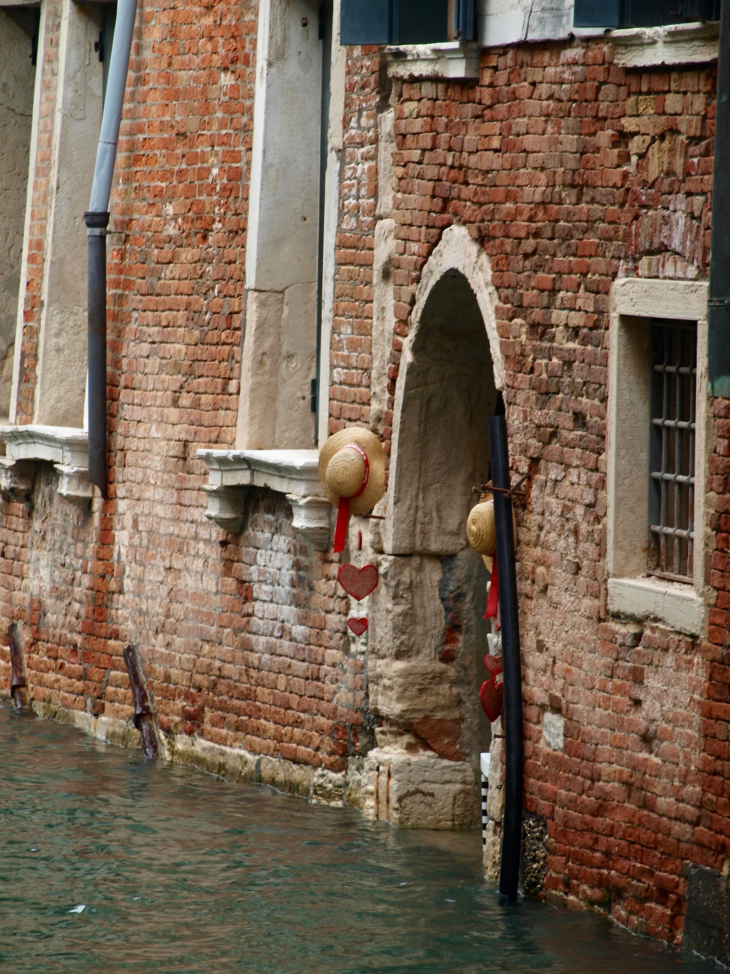 Façade en briques avec fenêtre, arche et décoration de cœurs en haut de l'ouverture, en bord d'eau.