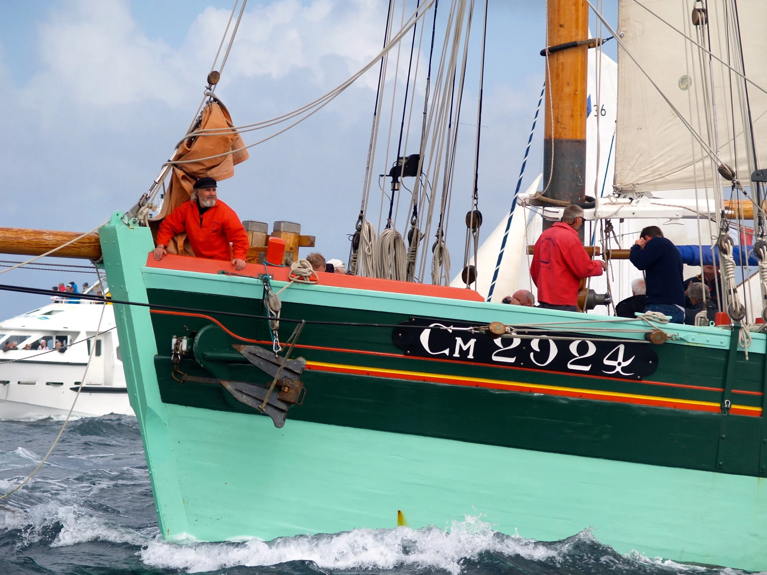 Un voilier avec des personnes à bord naviguant en mer, le ciel est en partie nuageux.