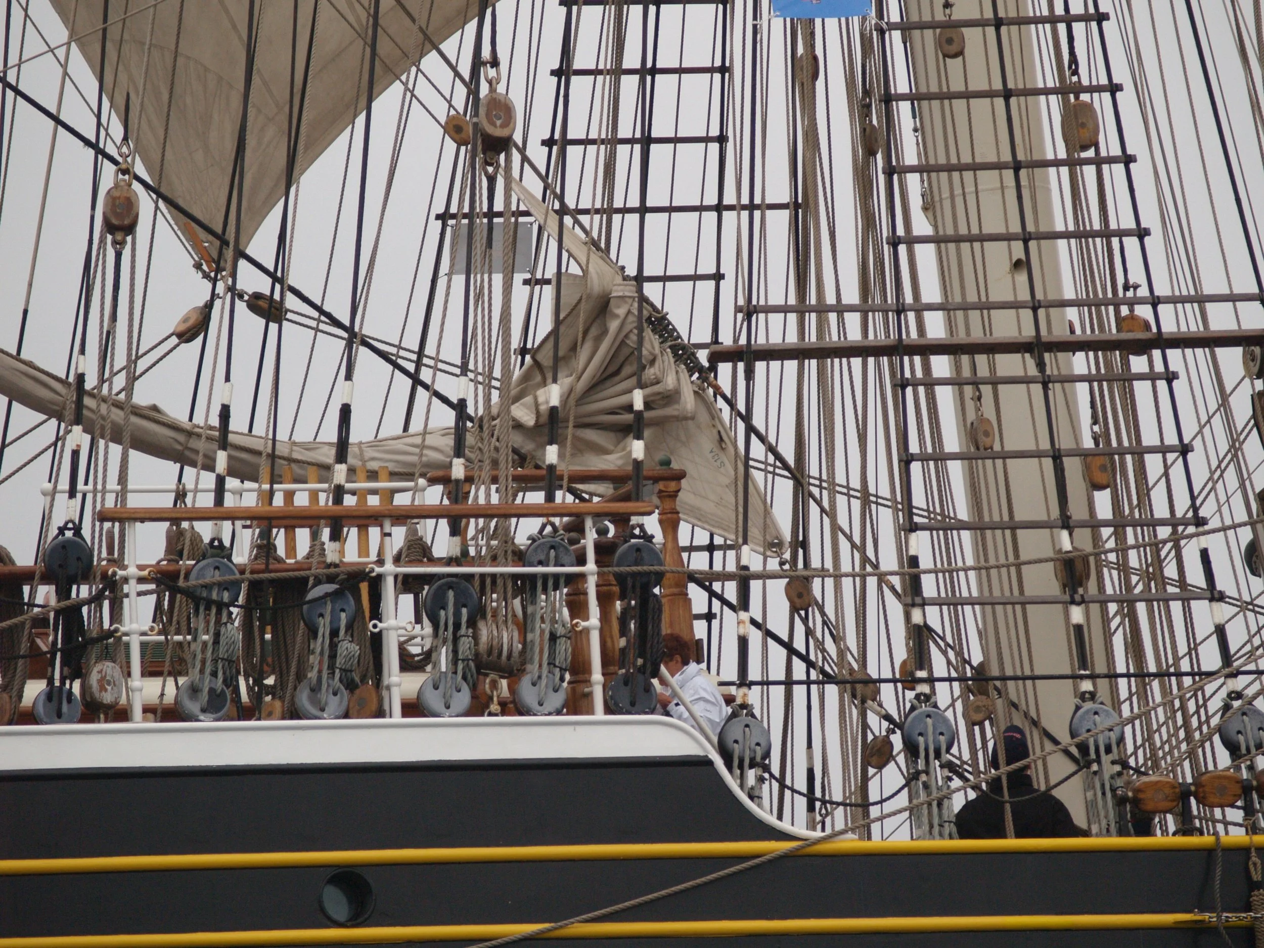 Photo d'un navire à voile avec ses cordages et ses mâts, vue de dessous, avec un ciel gris en fond.