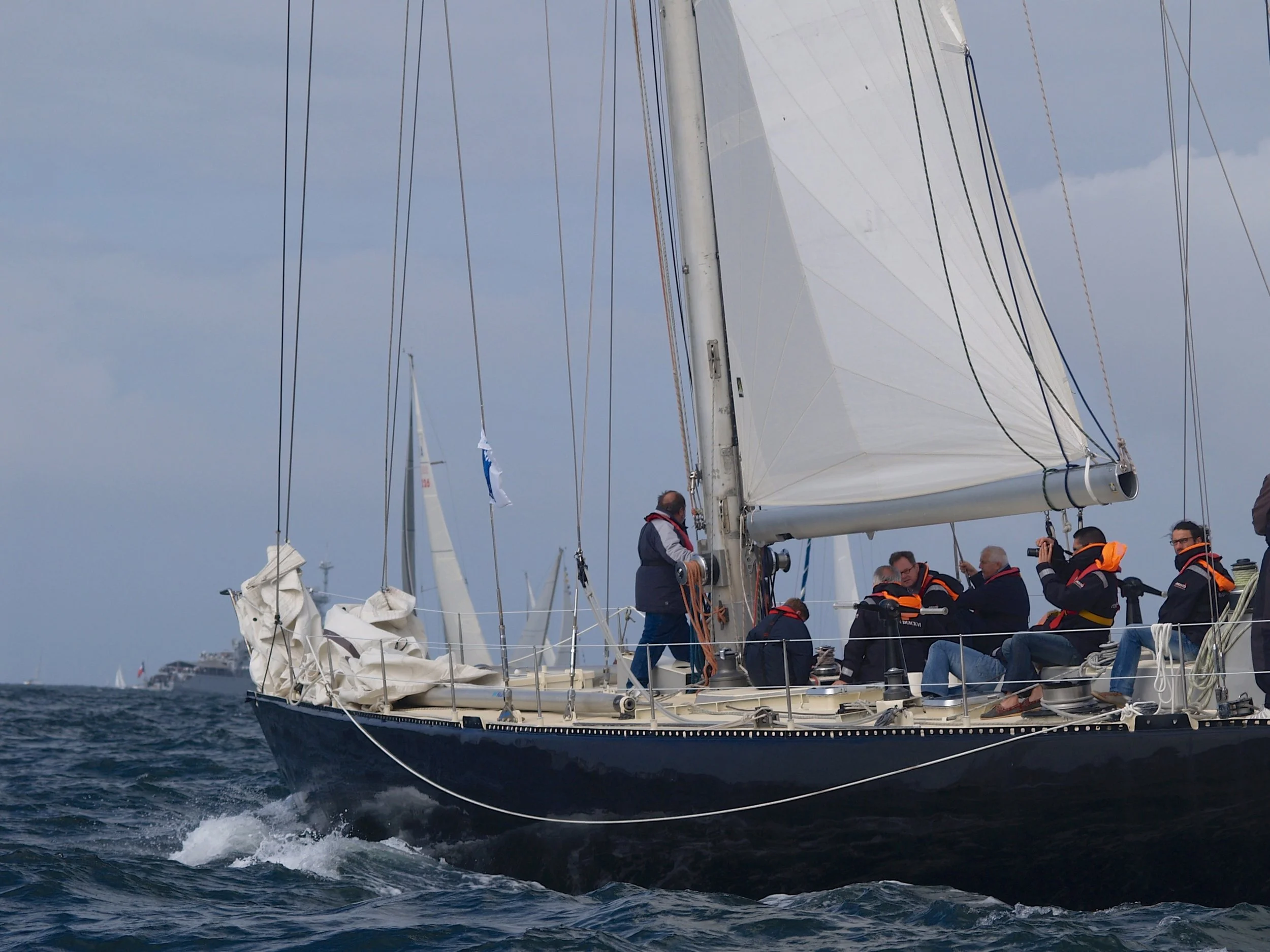 Un voilier avec plusieurs personnes à bord navigant sur la mer par une journée nuageuse.