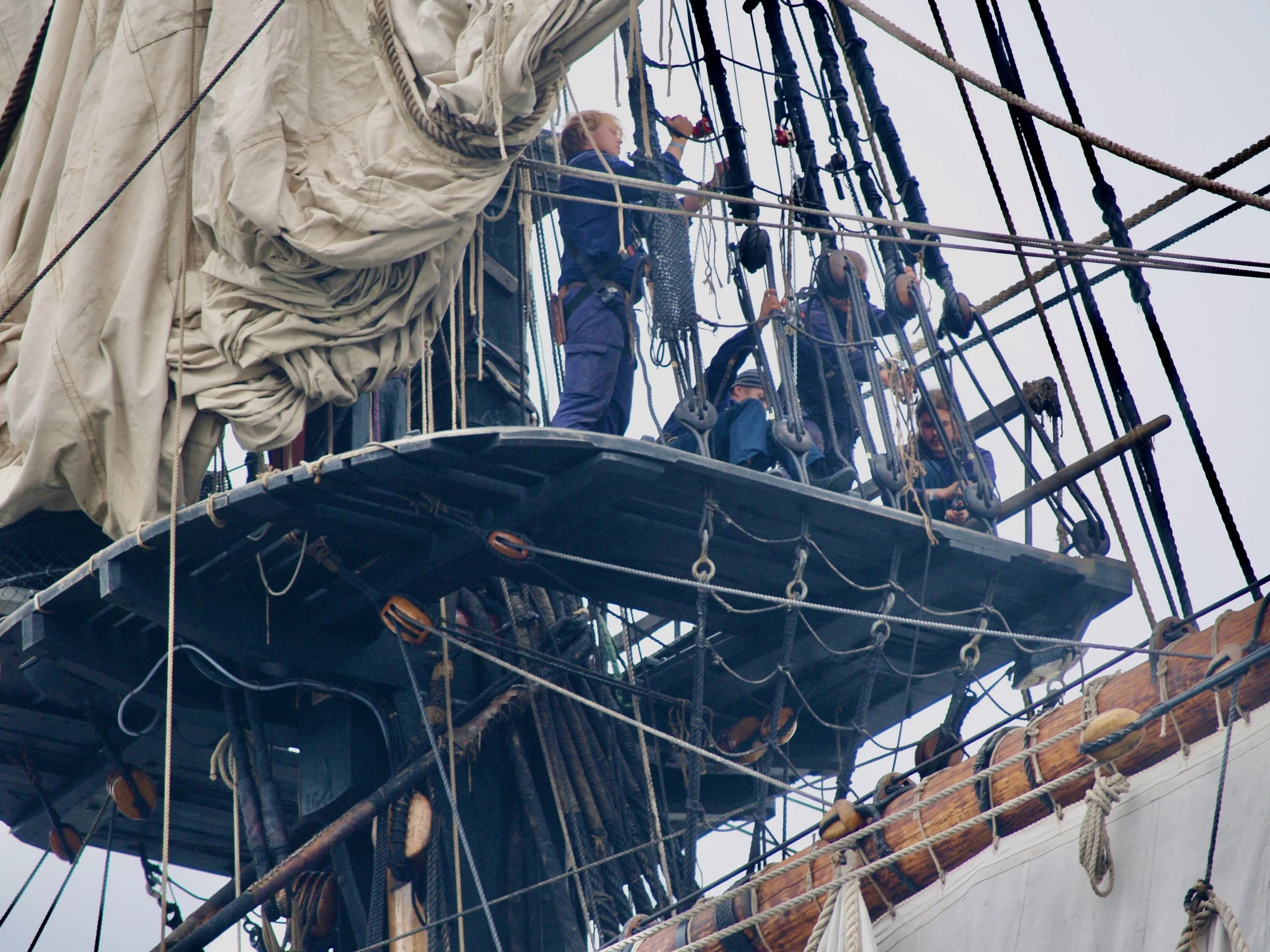 Des personnes apprennent à grimper une corde sur un bateau à voiles.