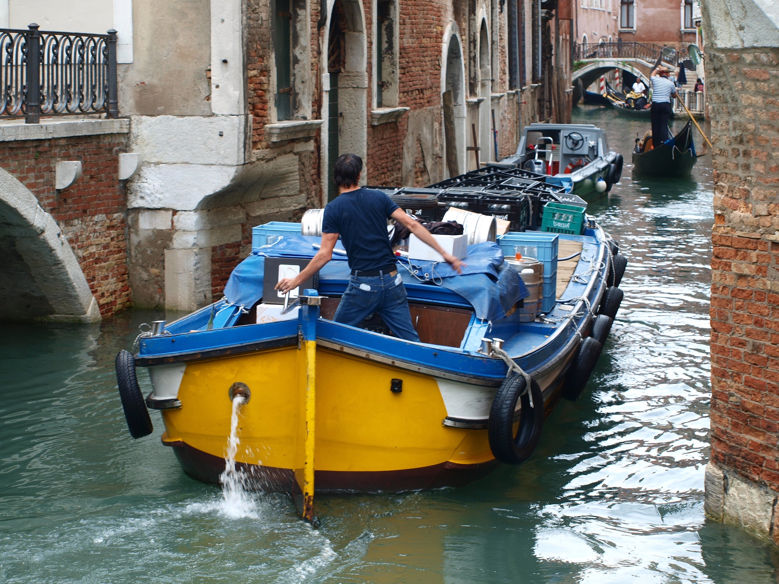 Un homme conduit un bateau avec des caisses de stockage sur un canal étroit à Venise, en Italie.