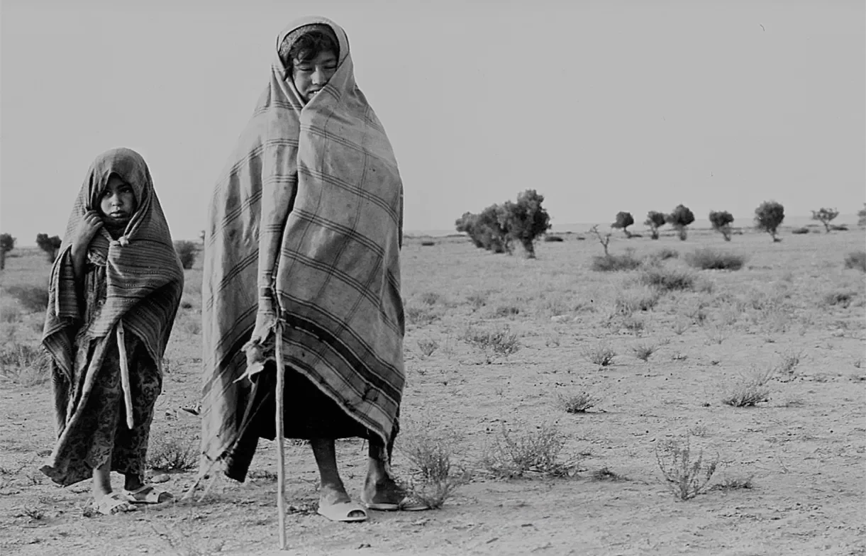 Deux enfants en vêtements traditionnels dans un paysage désertique avec quelques arbres.