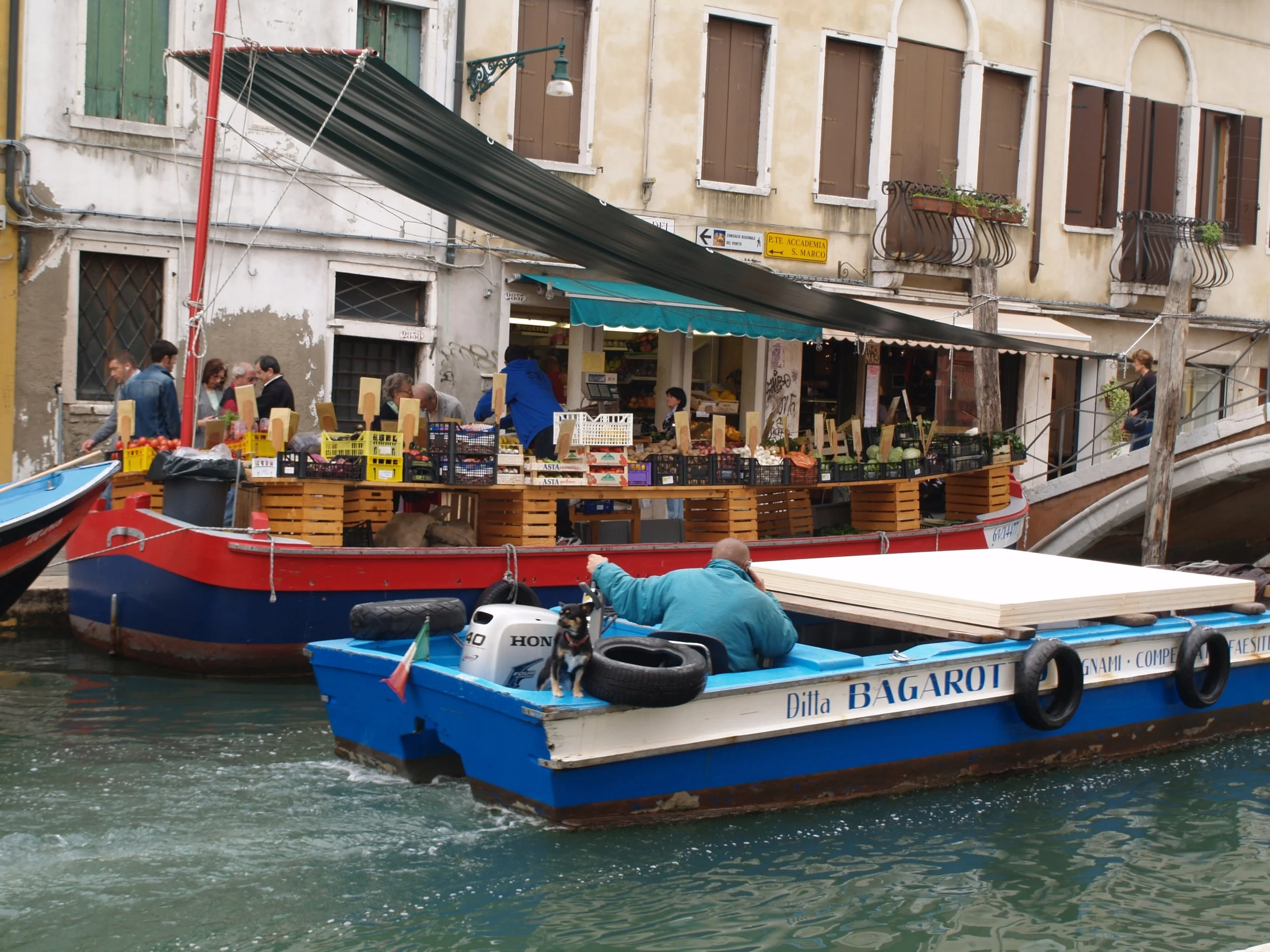 Bateau avec stand de fruits et légumes amarré dans un canal à Venise, avec bâtiment ancien en arrière-plan.