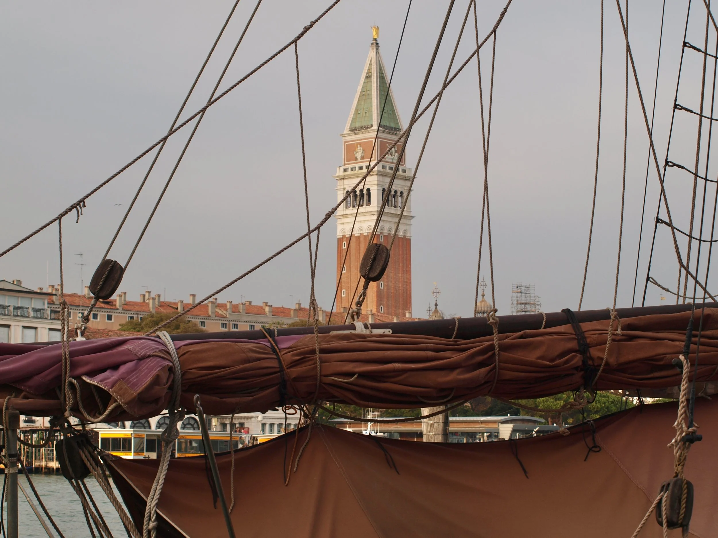 Vue d'une tour avec un sommet doré, vue depuis un bateau avec ses voiles en bois et ses câbles.