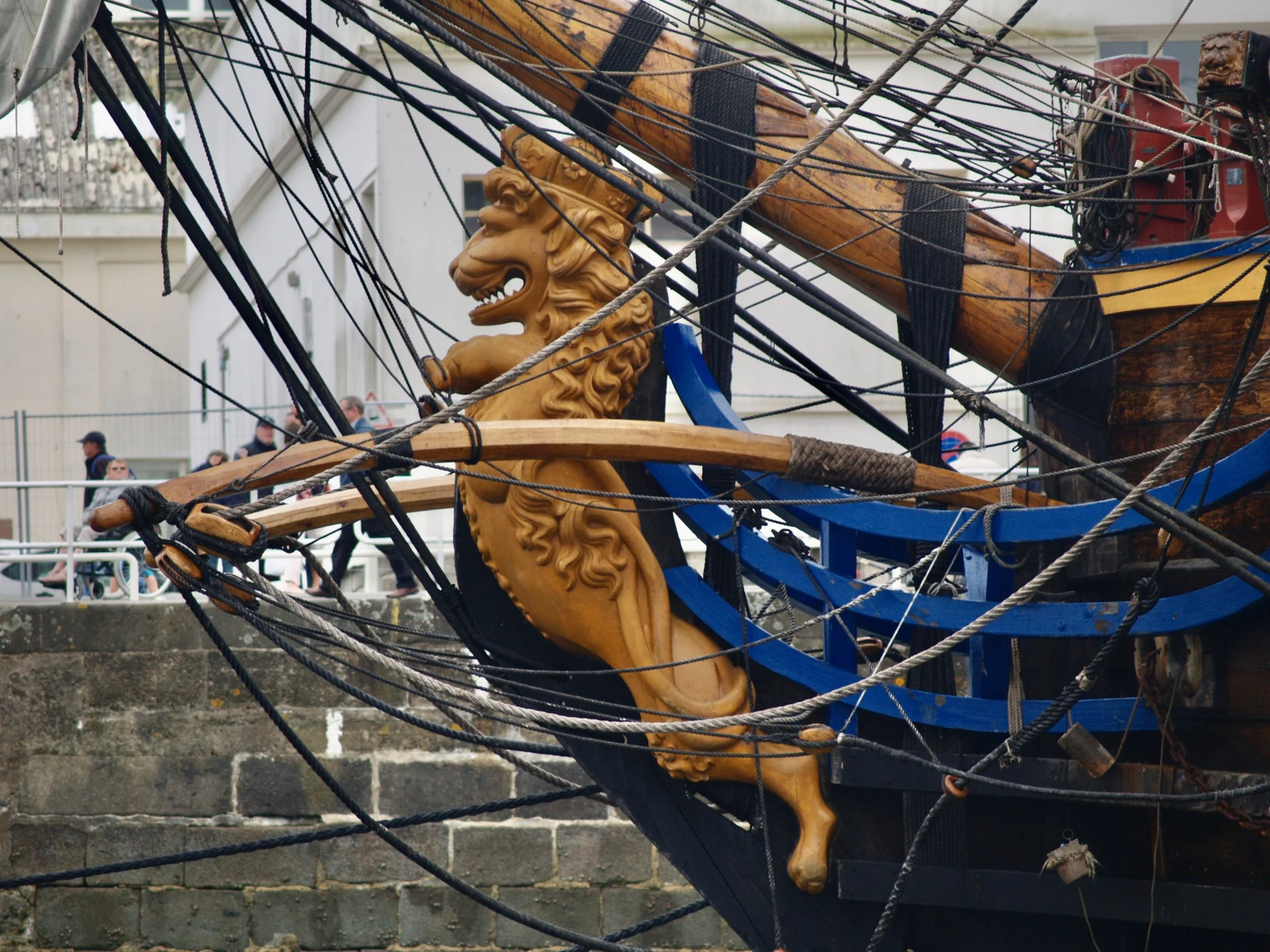 Une sculpture en bois représentant une tête de lion montée sur un bateau en bois, entouré de cordages et d'éléments en rigide noir.