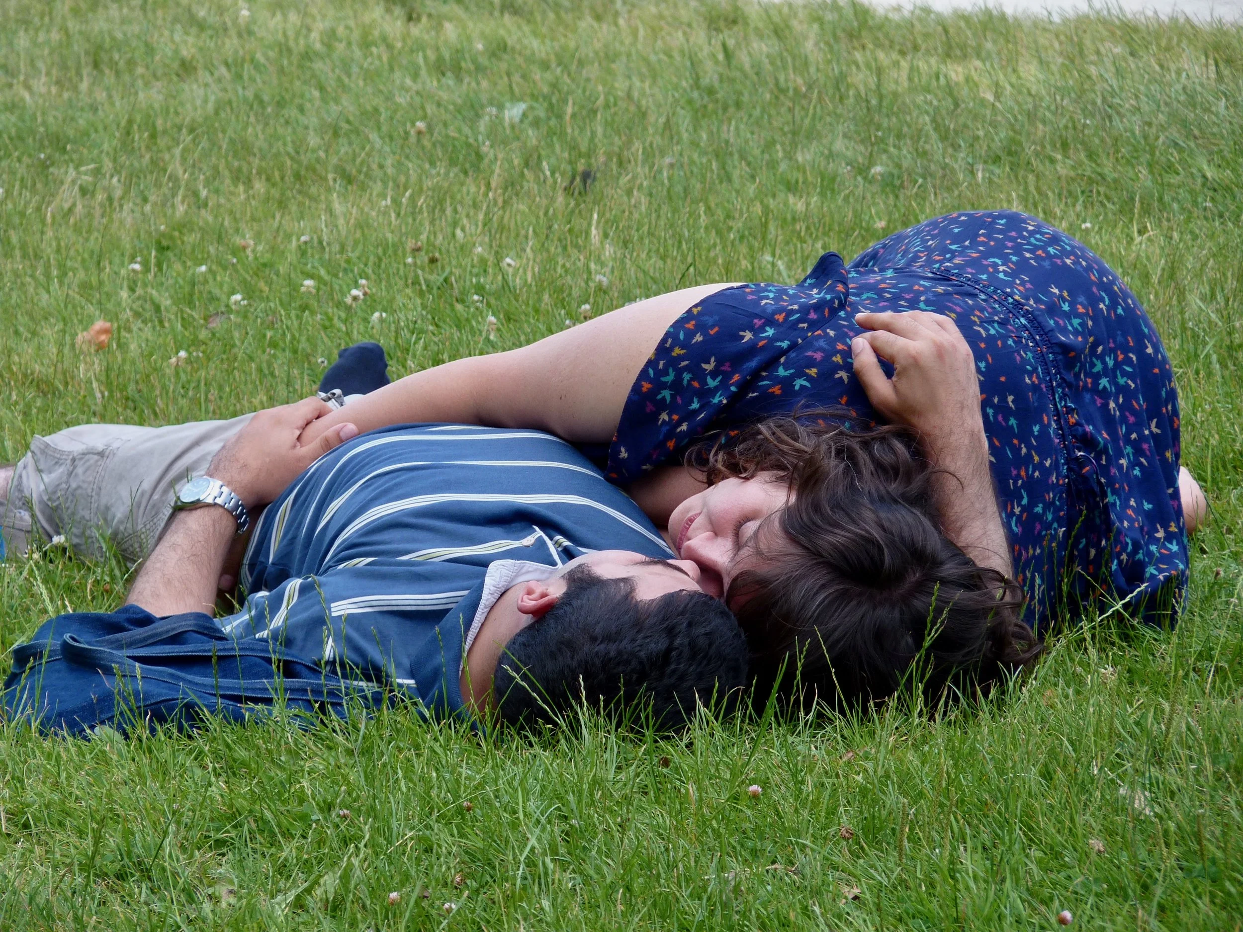 Deux personnes allongées sur l'herbe du parc, se tenant la main, un homme et une femme, semblant se détendre et profiter du moment ensemble.