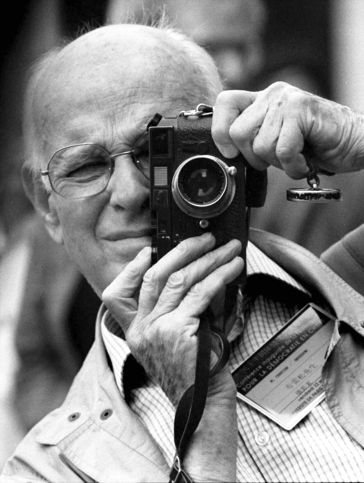 Un homme âgé avec des lunettes tient un appareil photo devant son visage, prenant une photo de lui-même.